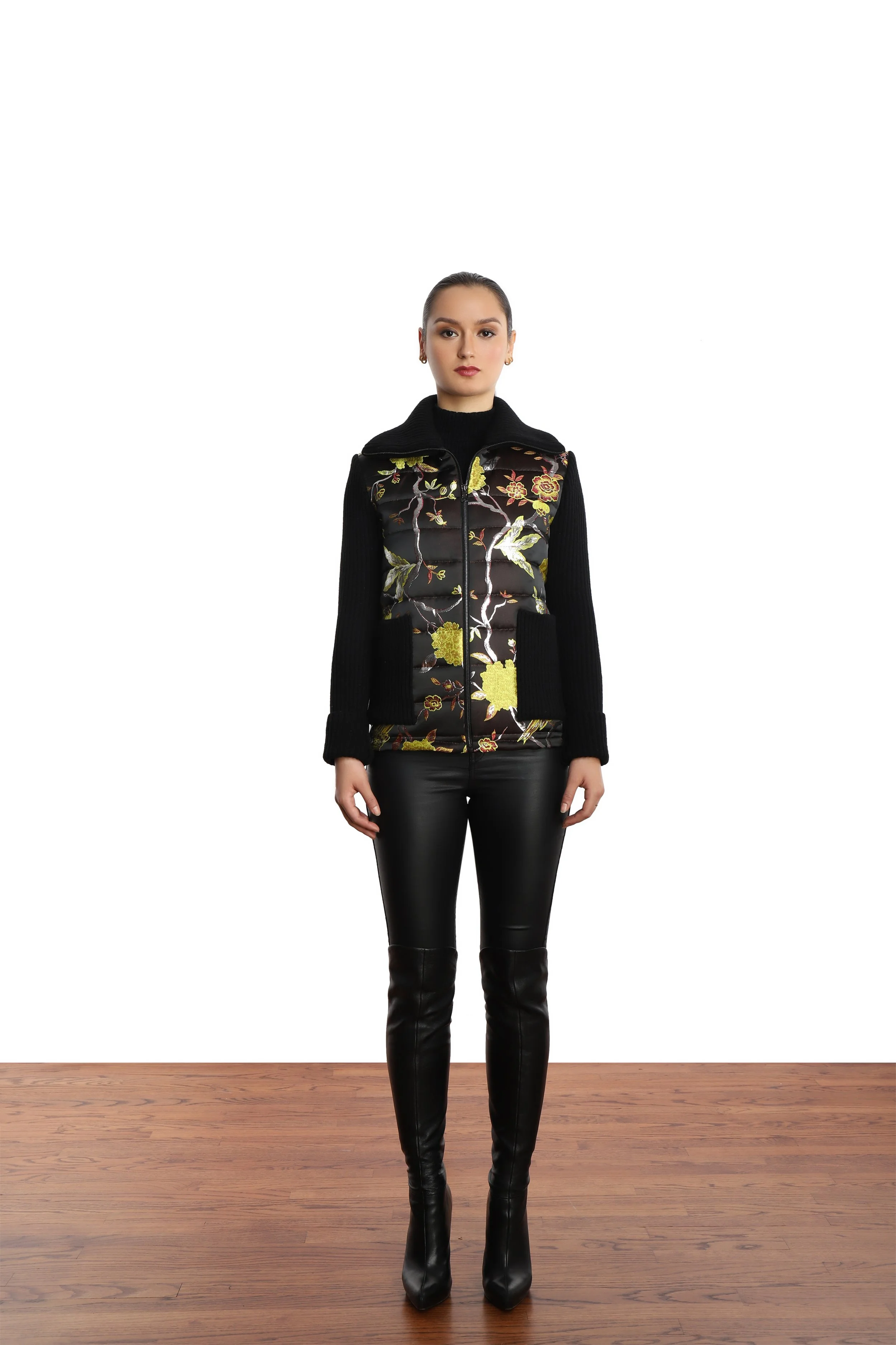 Model wearing a multi colored embroidered floral baseball jacket with black rib knit sleeves, leather like black leggins  and over the knee black boots.