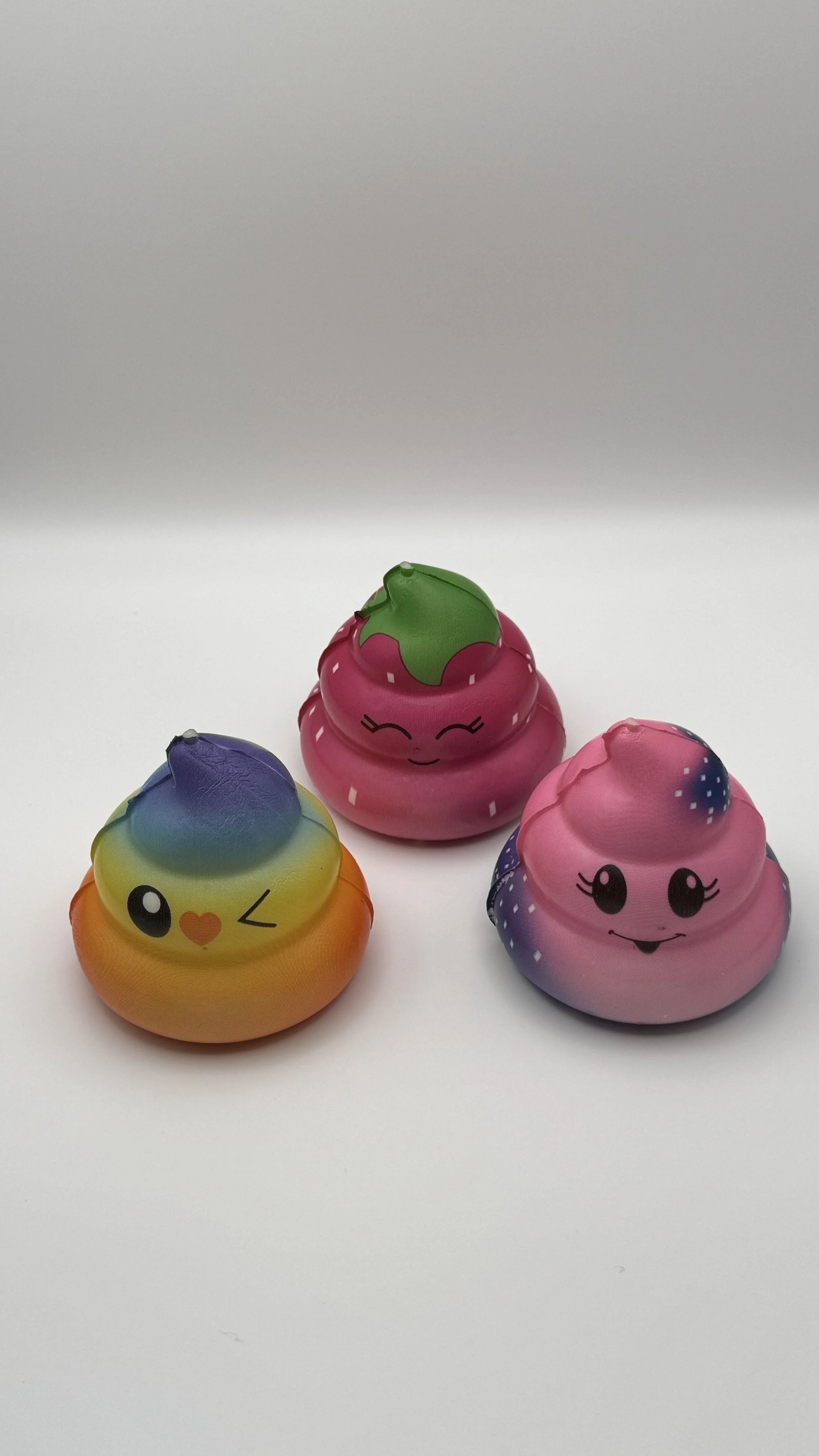 Colorful squishy toys with smiling and winking cartoon faces, designed to resemble strawberries and berries, placed on a white surface.