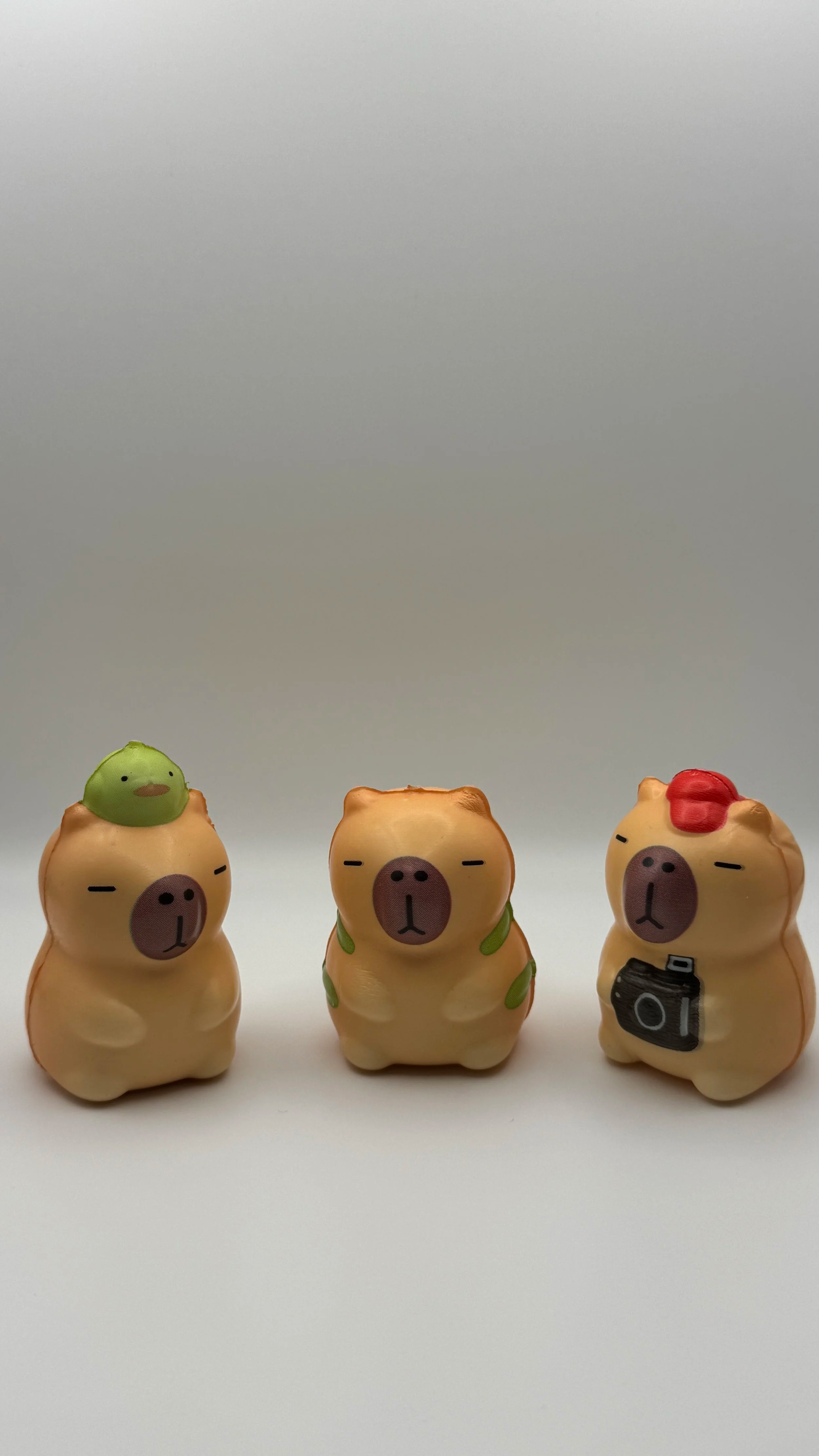 Three small pig figurines with different accessories, one with a bird on its head, one with leaves on its back, and one with a red hair and a camera, on a white surface against a plain background.