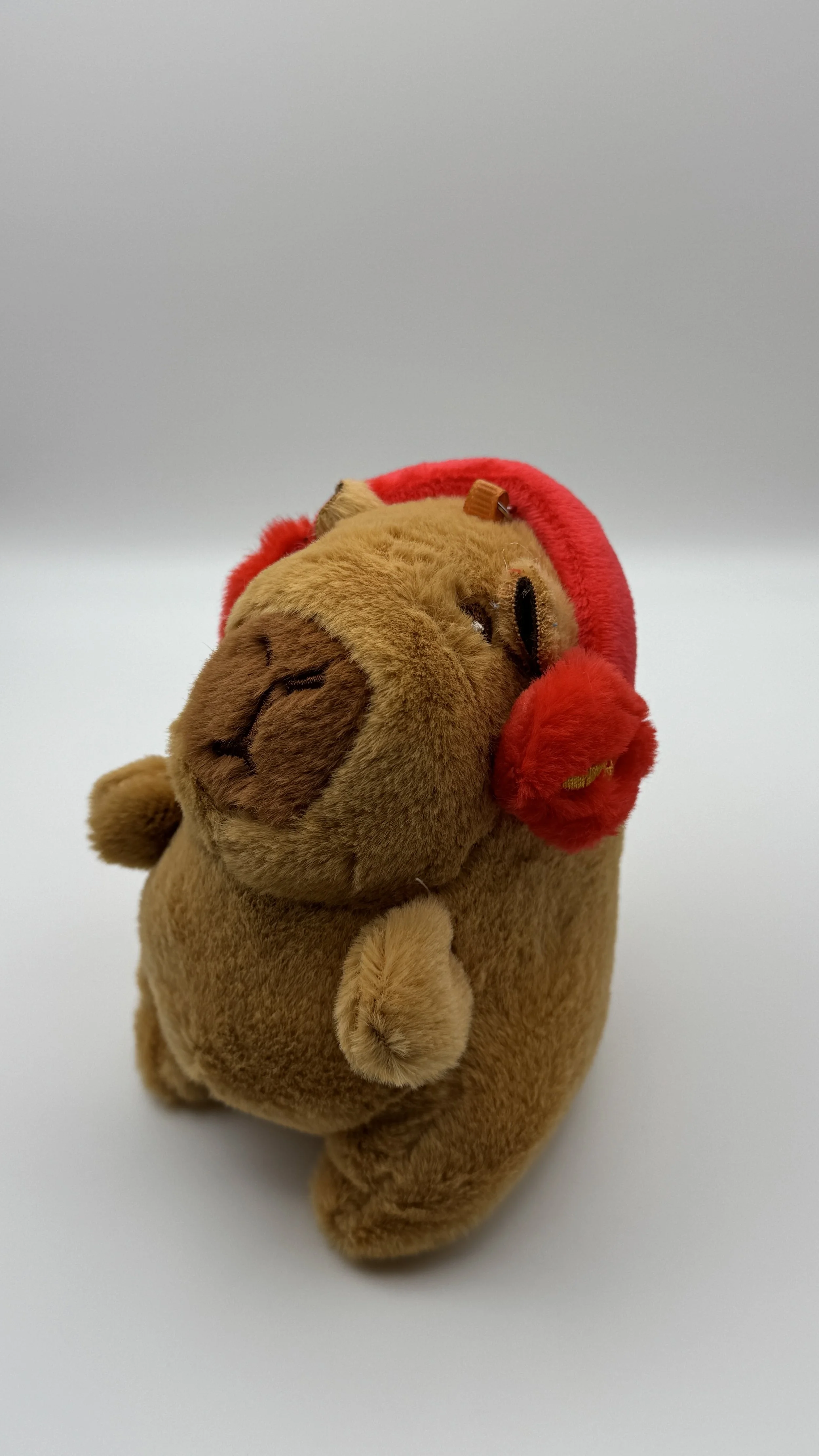 A plush toy of a monkey wearing red headphones, standing on a white surface with a plain, light-colored background.