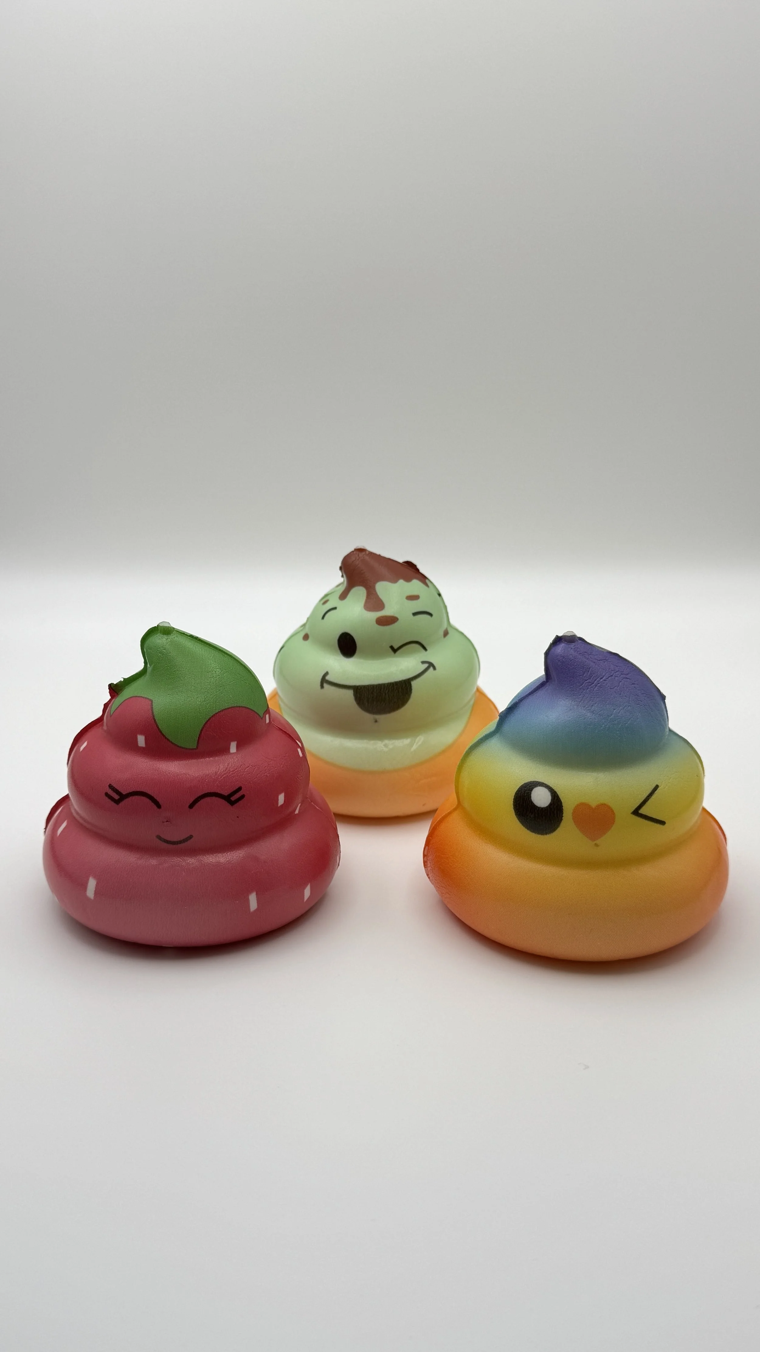 Three colorful squishy toys with cute, winking and smiling faces on a white background.