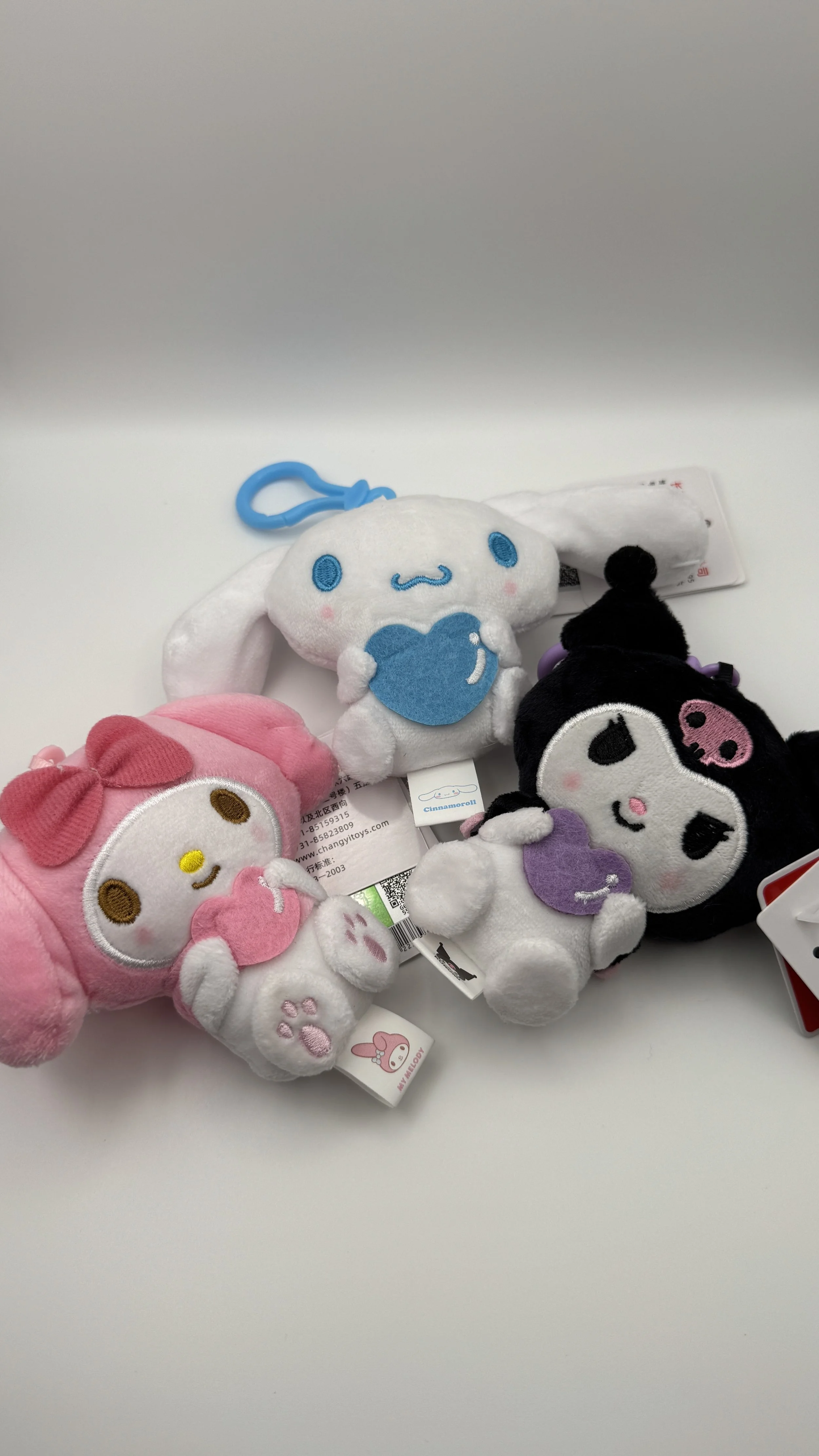 Four small plush keychains of popular Sanrio characters, My Melody, Cinnamoroll, Kuromi, and another character, on a white surface.