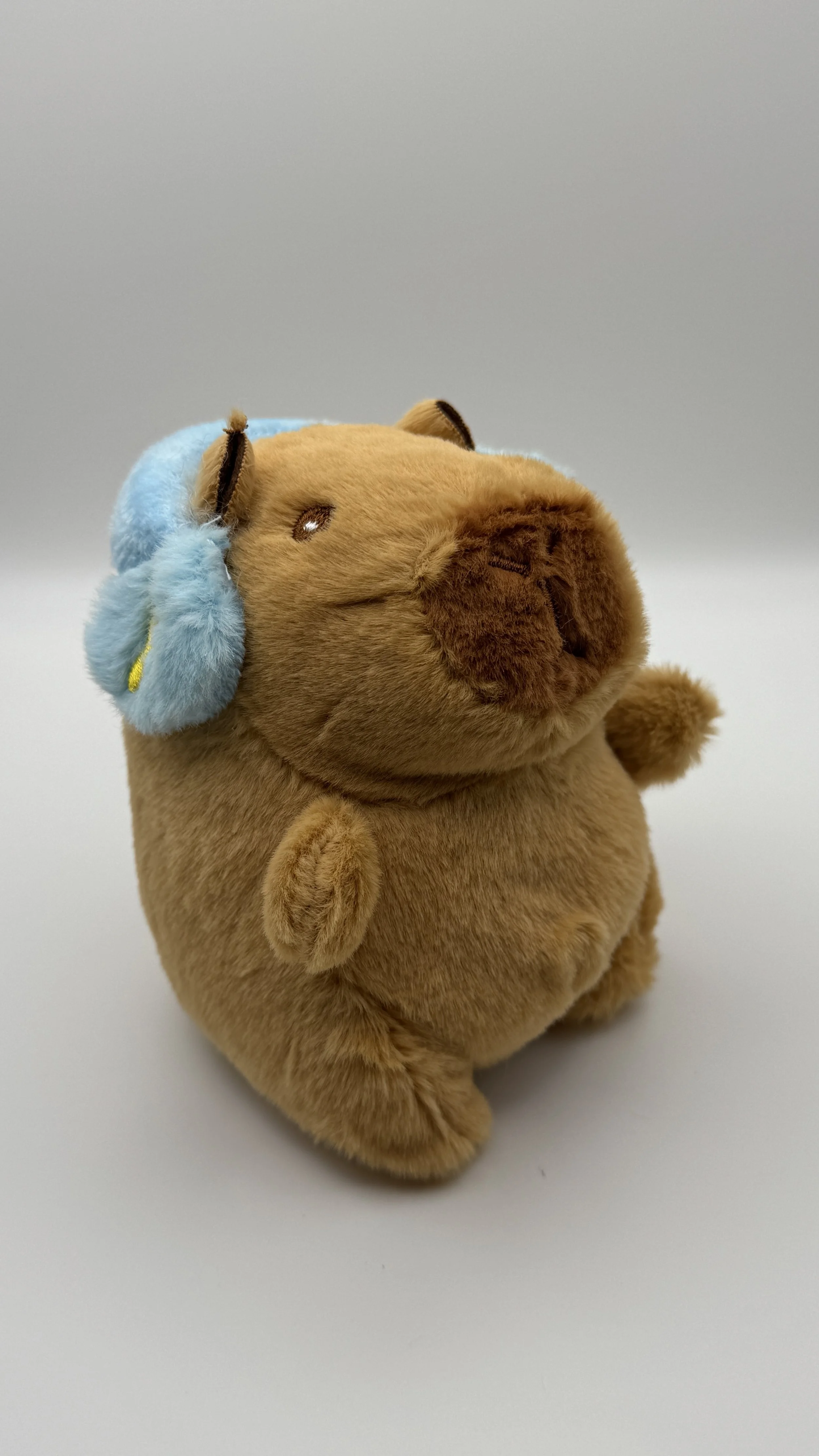 A plush toy of a hamster wearing blue headphones with yellow accents, sitting on a white surface against a plain gray background.
