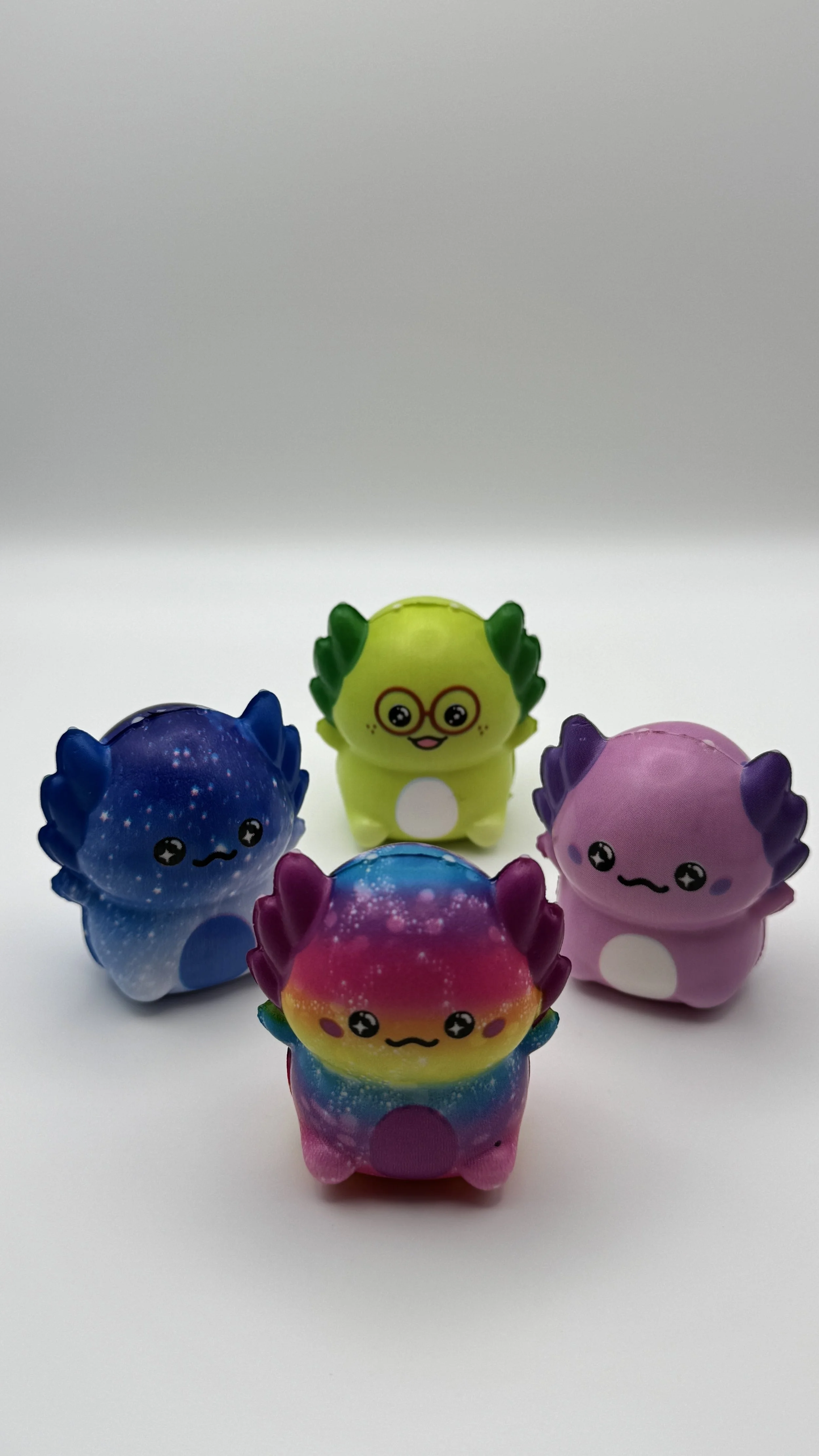 Four colorful, cute creature toys with starry and galaxy patterns, smiling faces, and circular patches on their bellies, arranged on a white surface against a white background.