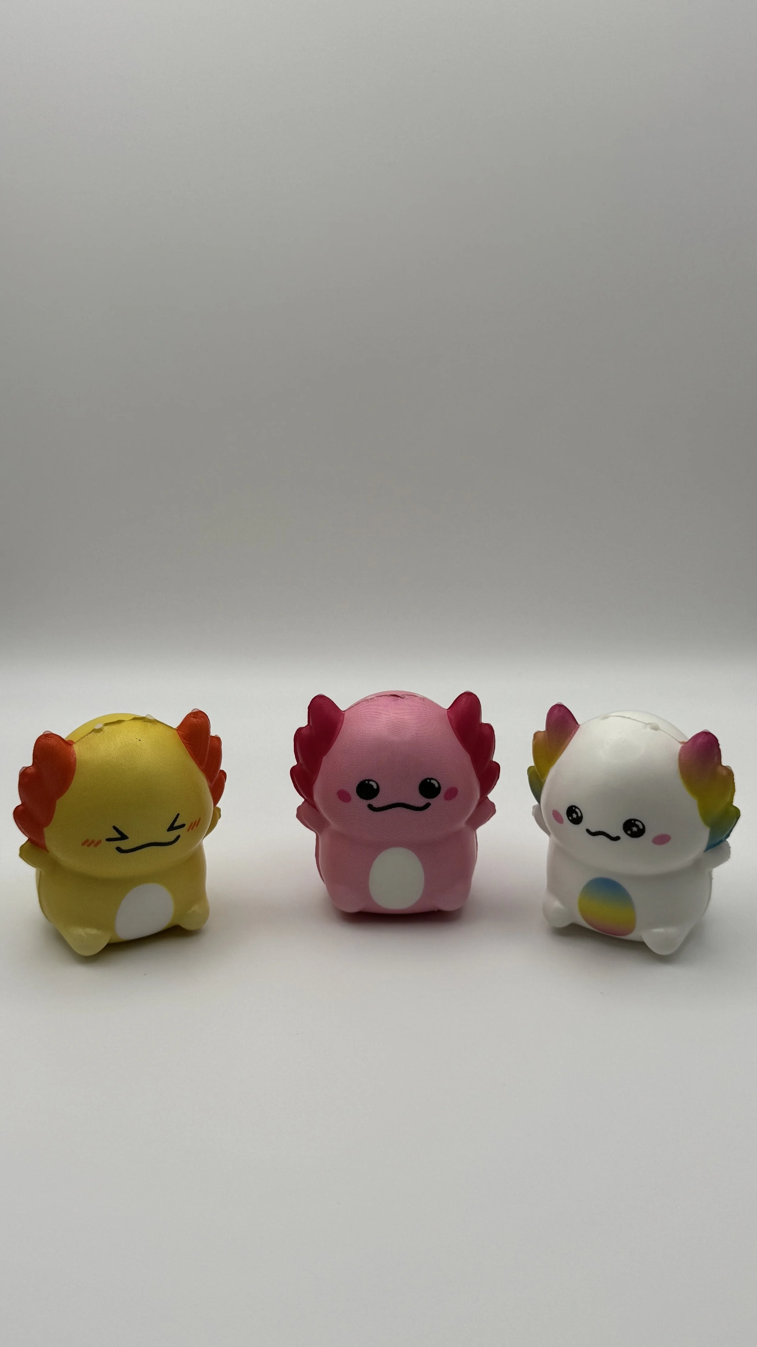 Three small, colorful, cartoon-like animal figurines with rainbow and rainbow-colored details on the ears and belly, placed on a white surface against a light gray background.