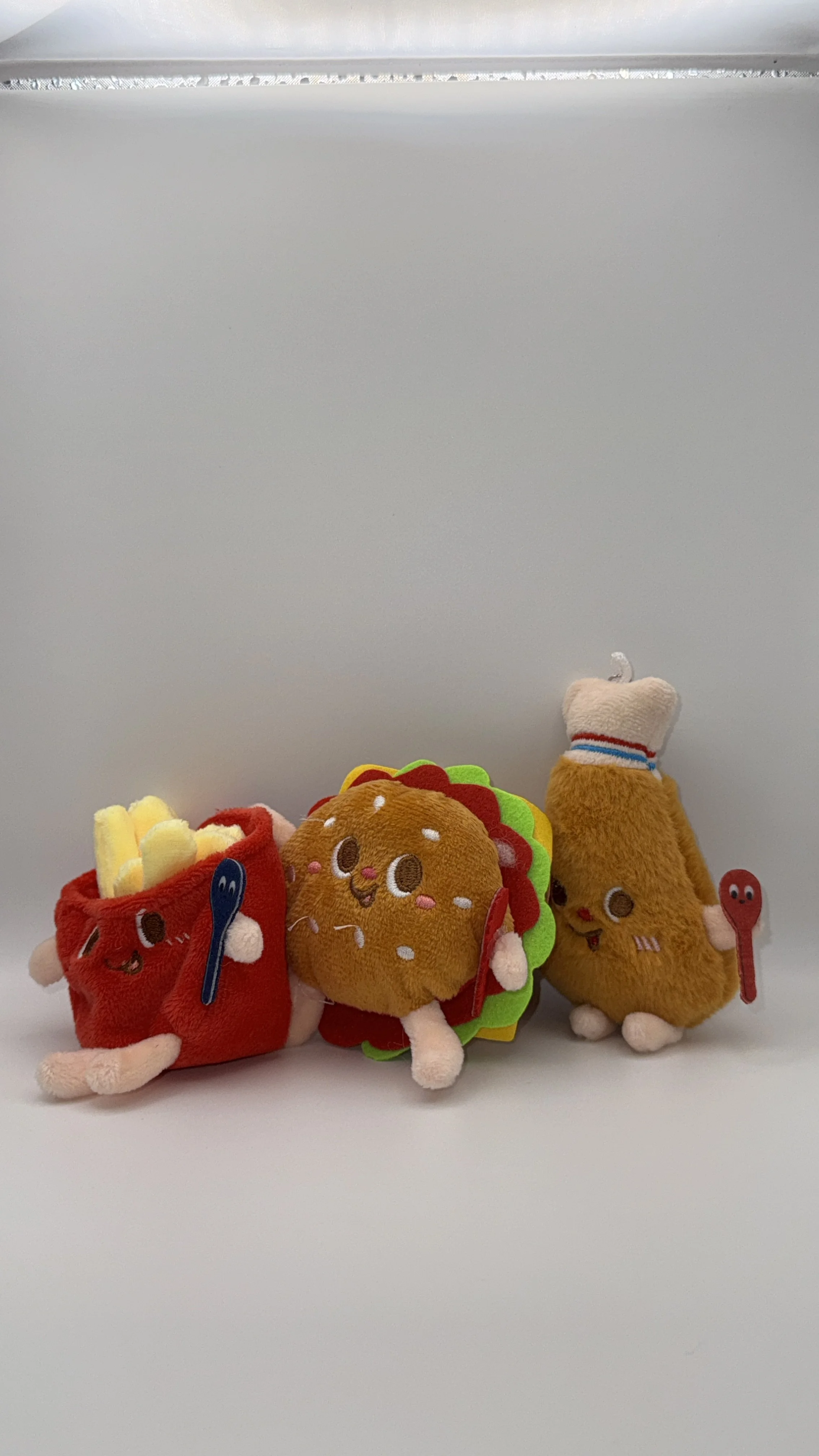Three plush toys resembling food with happy faces, sitting on a white surface against a plain white background.