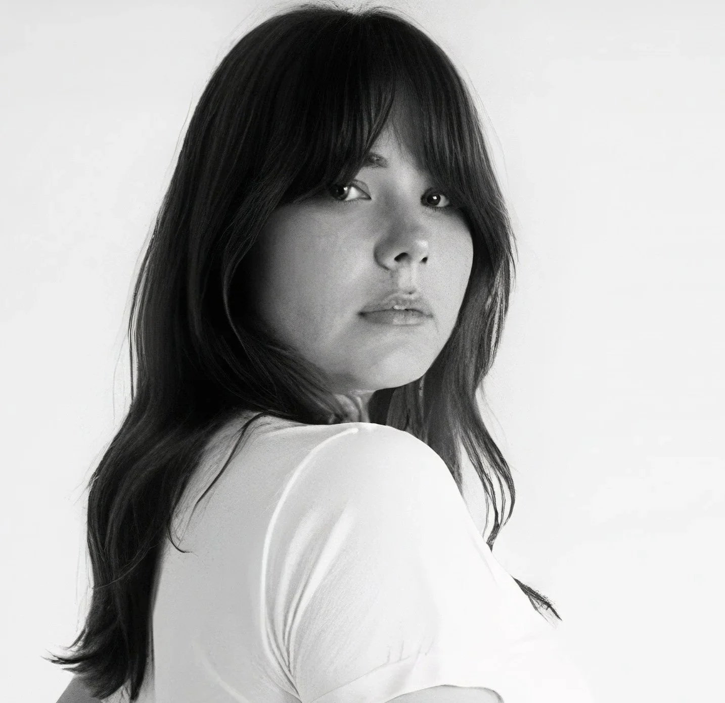 Black and white portrait of a woman with shoulder-length dark hair, looking over her shoulder at the camera.