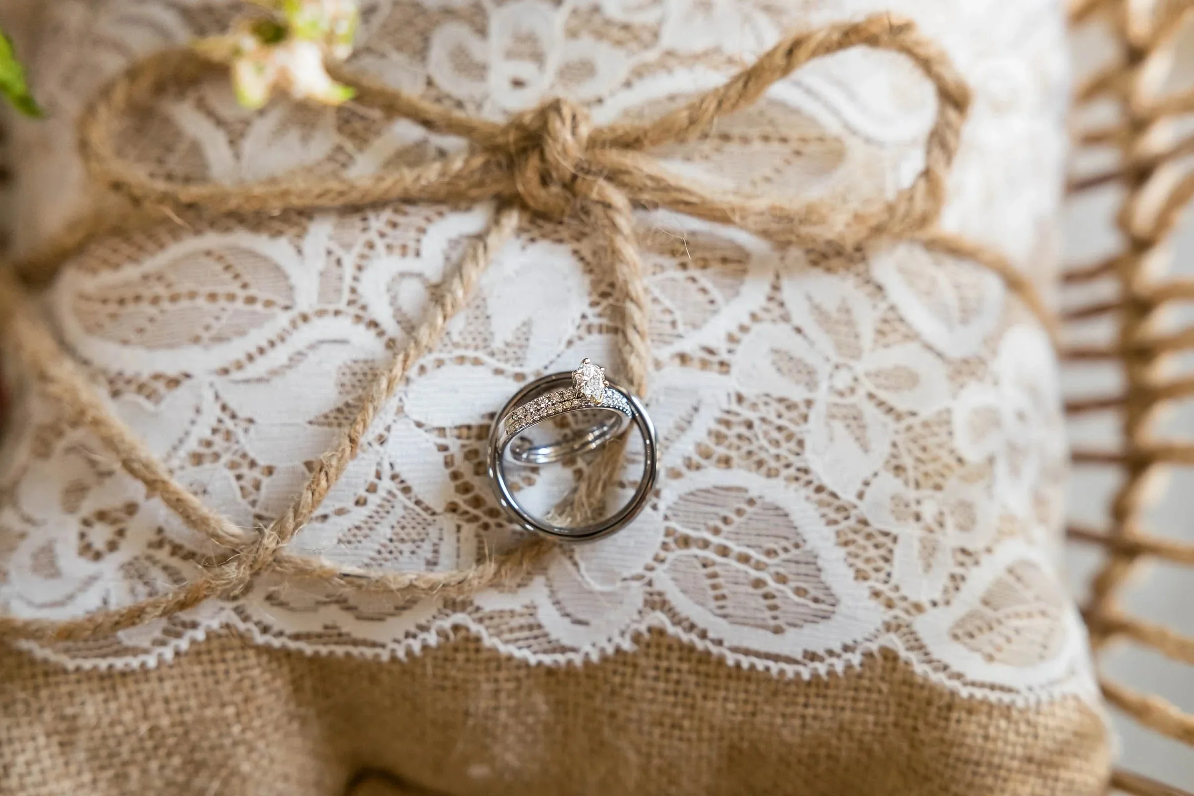 Engagement ring with diamond and wedding band with small diamonds resting on burlap and lace wrapped with twine.