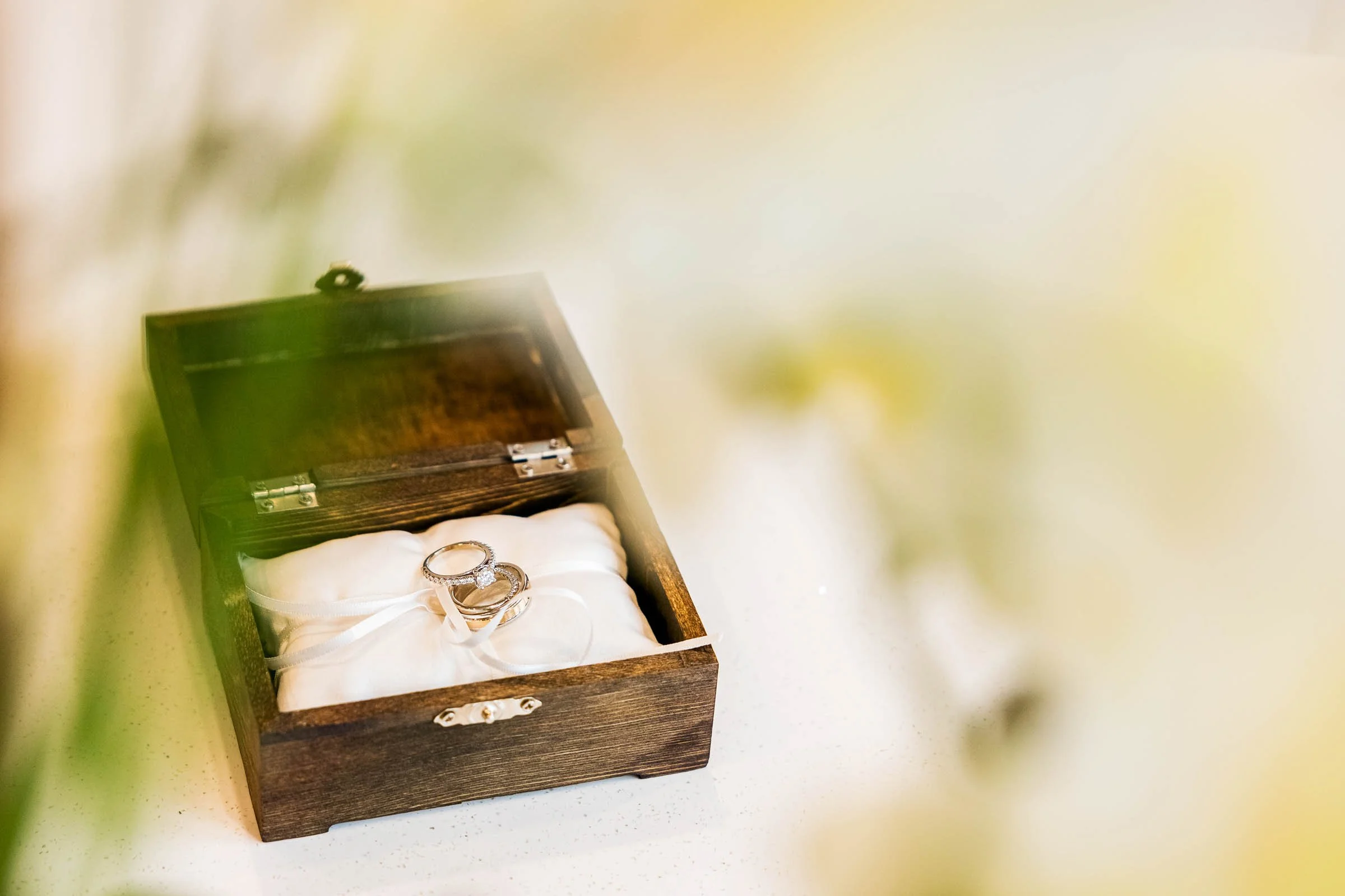 Wooden jewelry box containing a pair of wedding rings resting on white fabric.
