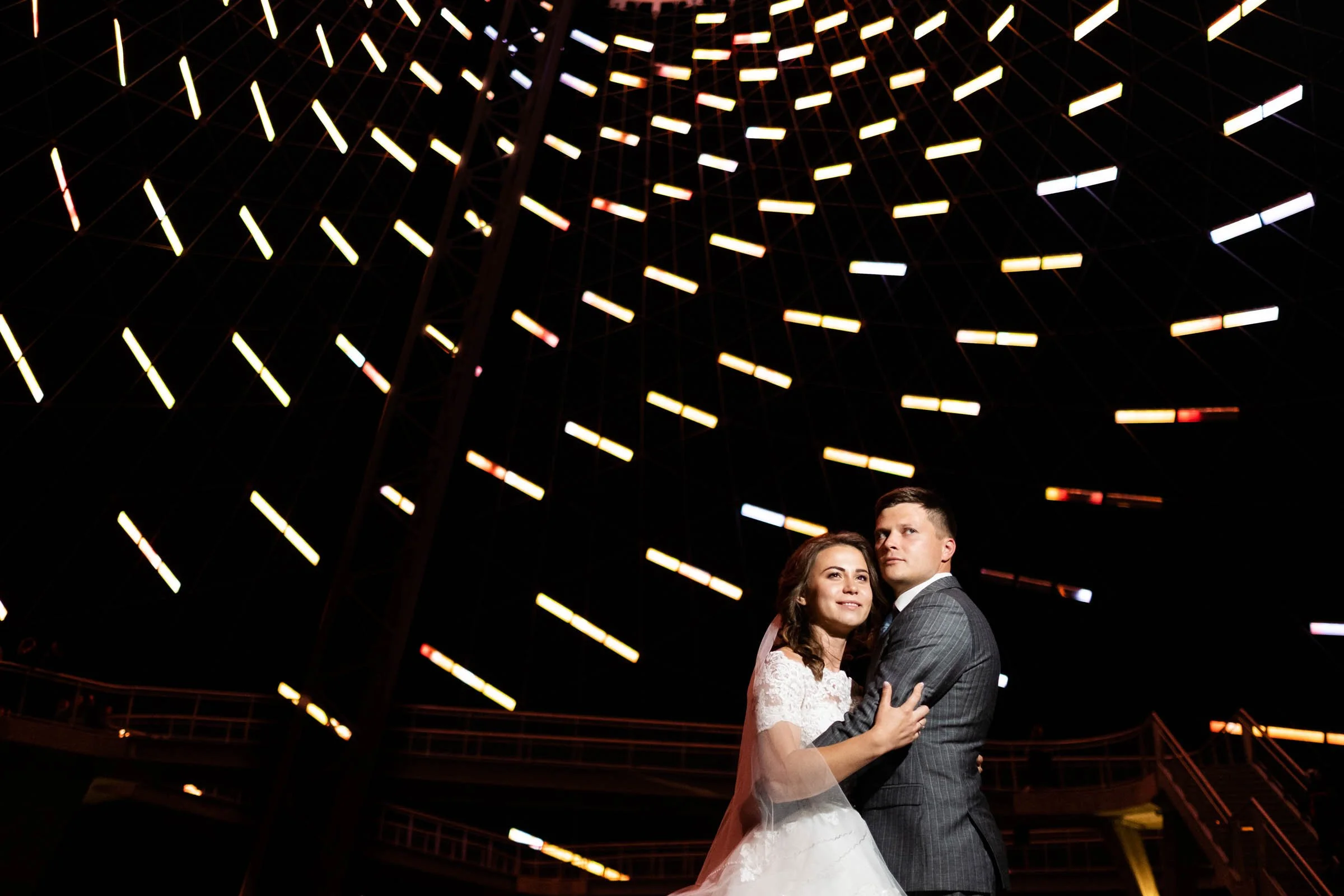A bride and groom sharing a dance at night under a large illuminated Ferris wheel.
