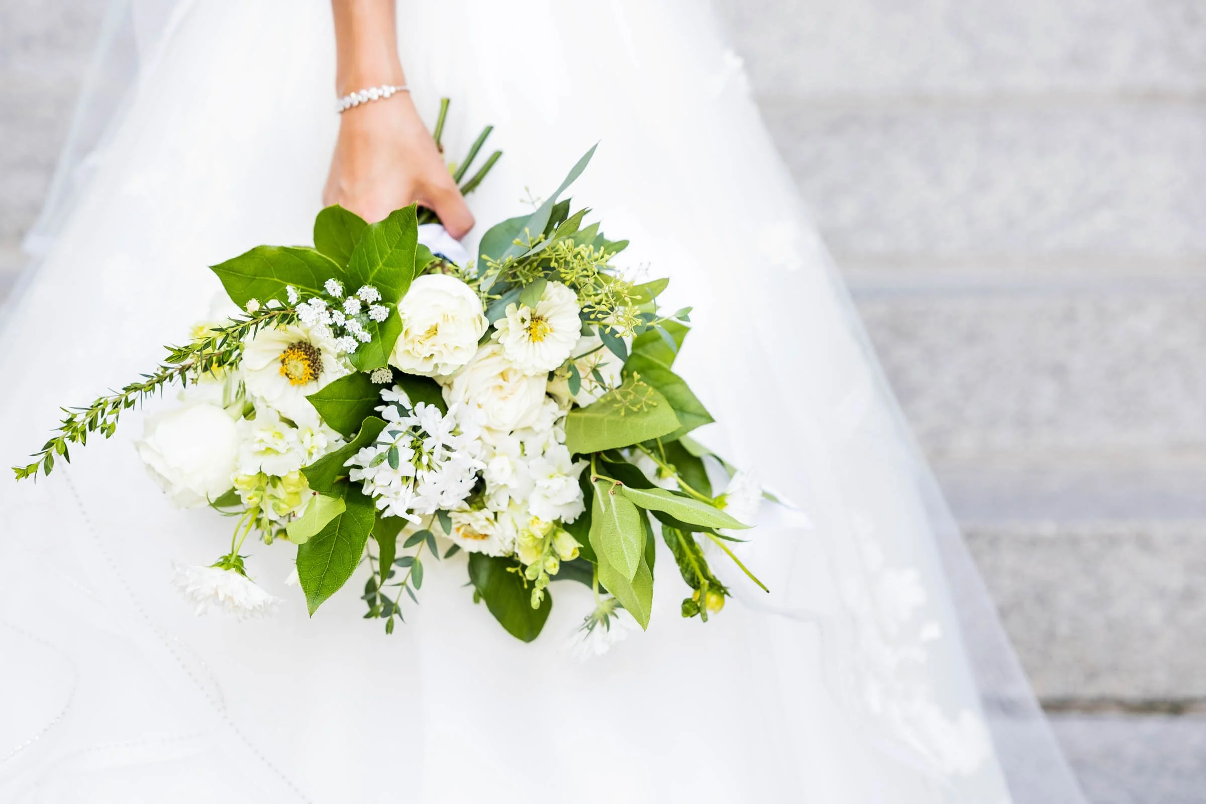 A bride holding a bouquet of white and green flowers on her wedding day.