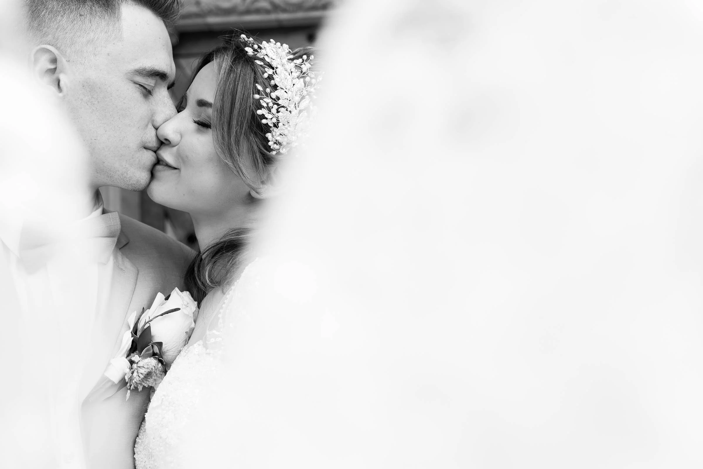 A black and white photo of a bride and groom kissing closely, with the bride wearing a floral headpiece. Spokane wedding photographer.