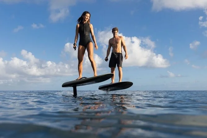 A man and woman stand on paddleboards in the ocean under a blue sky with clouds.