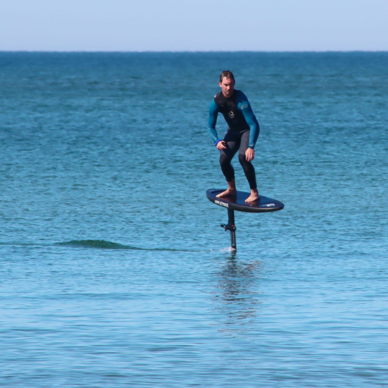 Person riding a flyboard over the water, wearing a wetsuit on a sunny day.