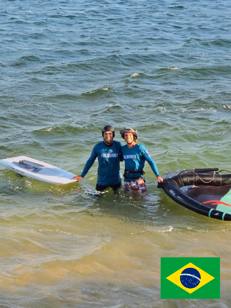 A young man with dark skin sitting on a bench against a beige wall, wearing a gray polo shirt and cream-colored pants, with a shadow cast on the wall behind him.