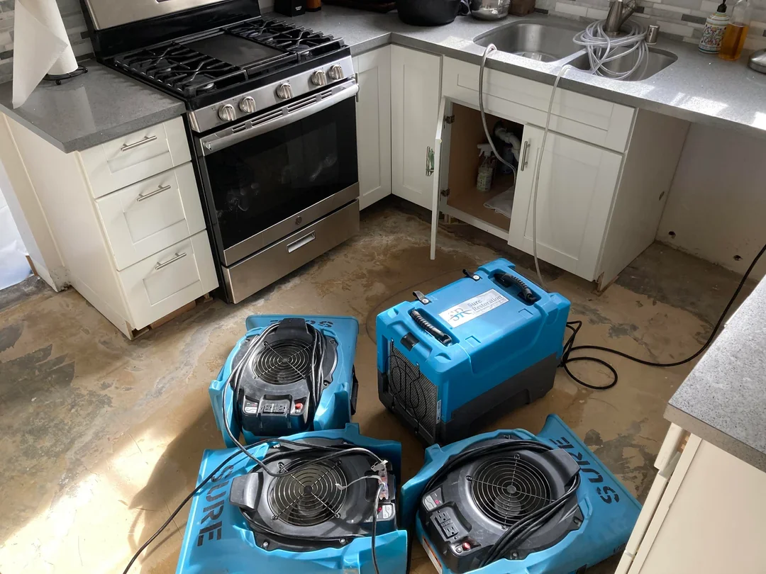 Kitchen with a stove, white cabinets, damaged cabinet under the sink, and three climate control kits on the floor.