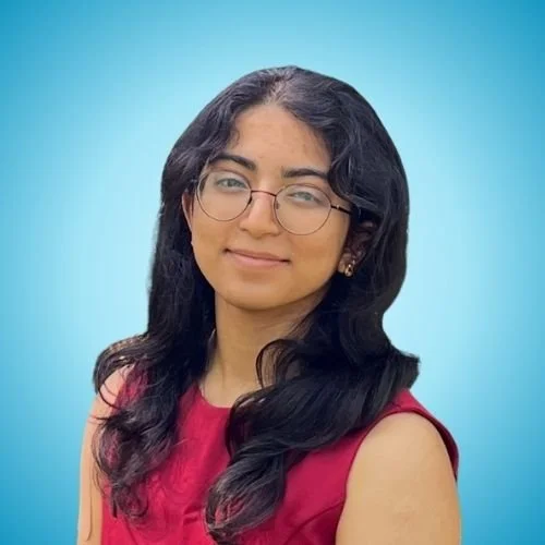A young woman with long black hair, glasses, and a pink sleeveless top posing against a blue background.