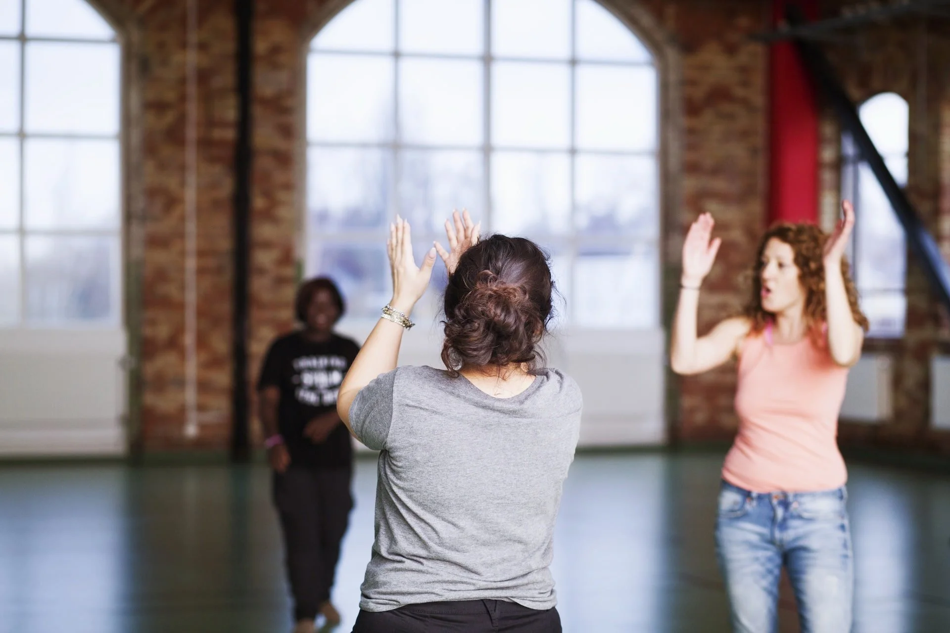 People practicing dance or aerobics in a brick-walled studio with large windows, engaging in a group activity.
