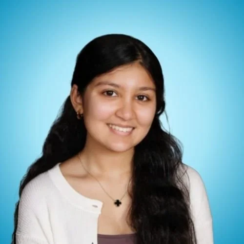 Young woman with long dark hair smiling, wearing a white cardigan and a necklace with a black pendant, against a blue background.