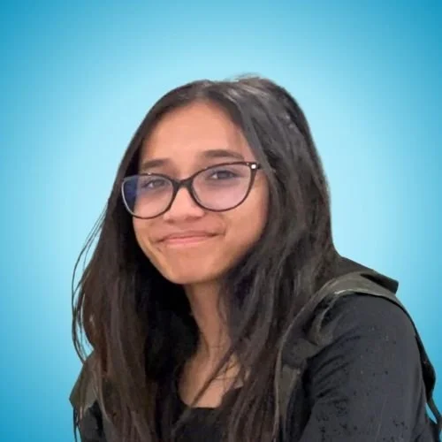 A young woman with glasses and long dark hair, smiling with a slight smirk, wearing a black shirt and backpack, against a light blue background.