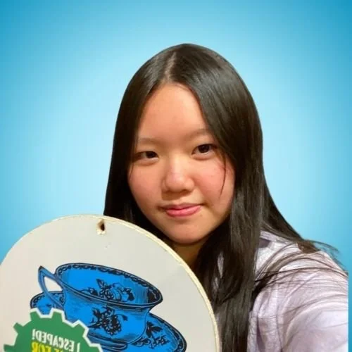 Young woman with long dark hair holding a decorative blue and black hat against a light blue background.