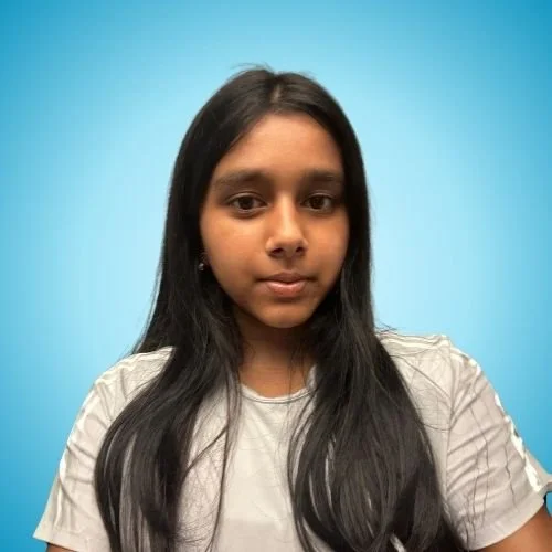 A young woman with long black hair and medium skin tone, wearing a light-colored shirt, standing against a solid light blue background.