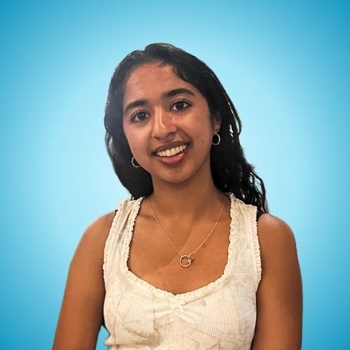 A young woman with long black hair, wearing a light-colored sleeveless top and jewelry, smiling against a blue background.