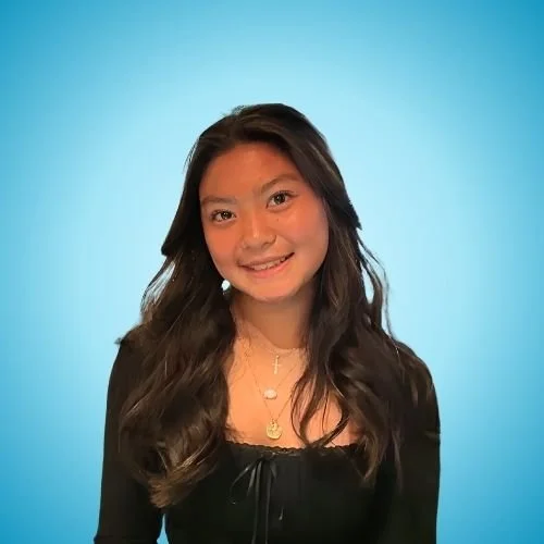 A young woman with long wavy dark hair smiling against a blue background.