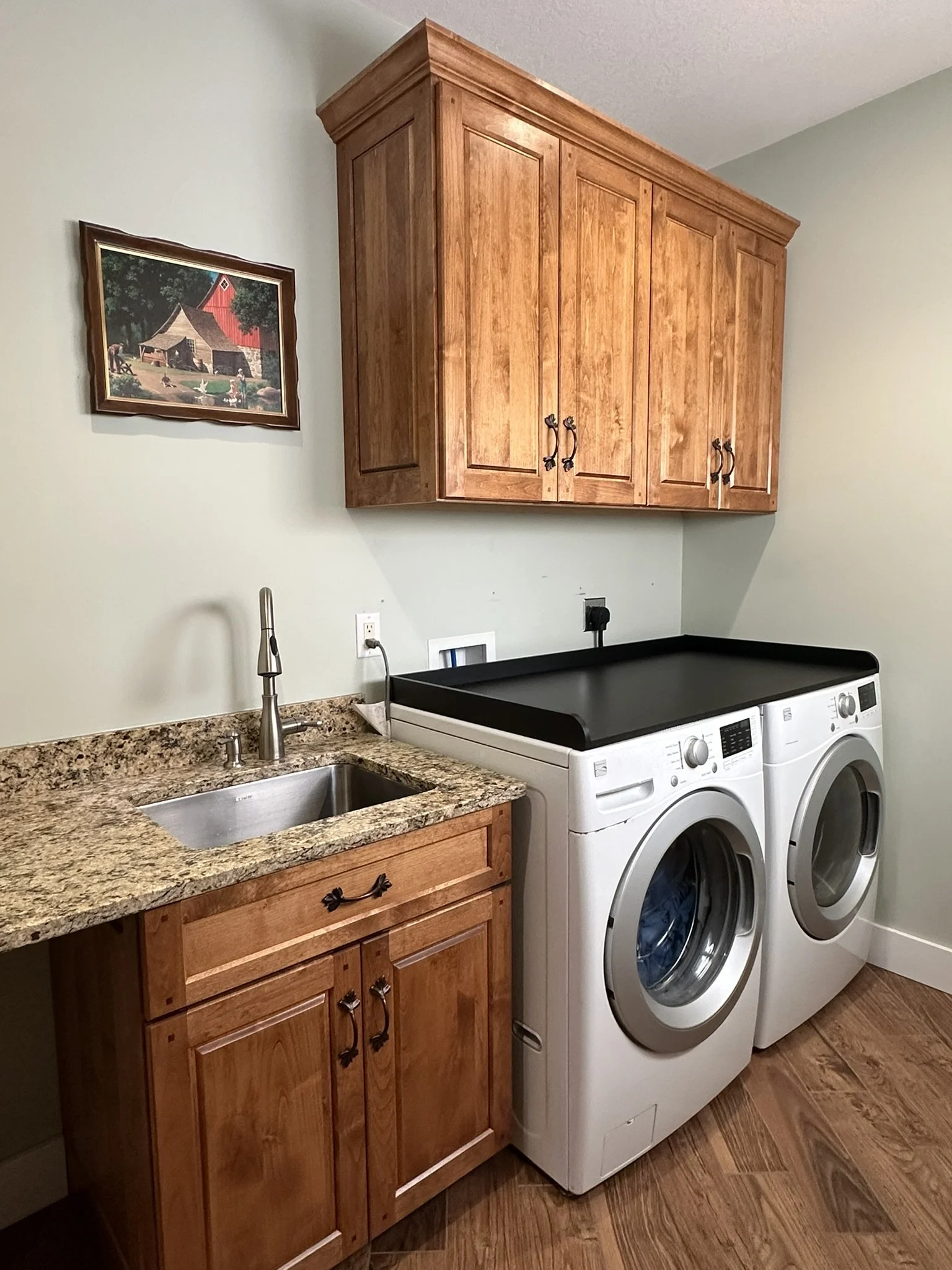 A laundry room with wooden cabinets, a granite countertop, a small sink, and a washer and dryer side by side.