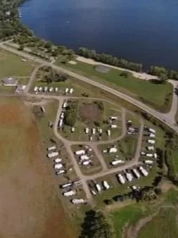 Aerial view of a campground near a large body of water with campsites, vehicles, and roads.