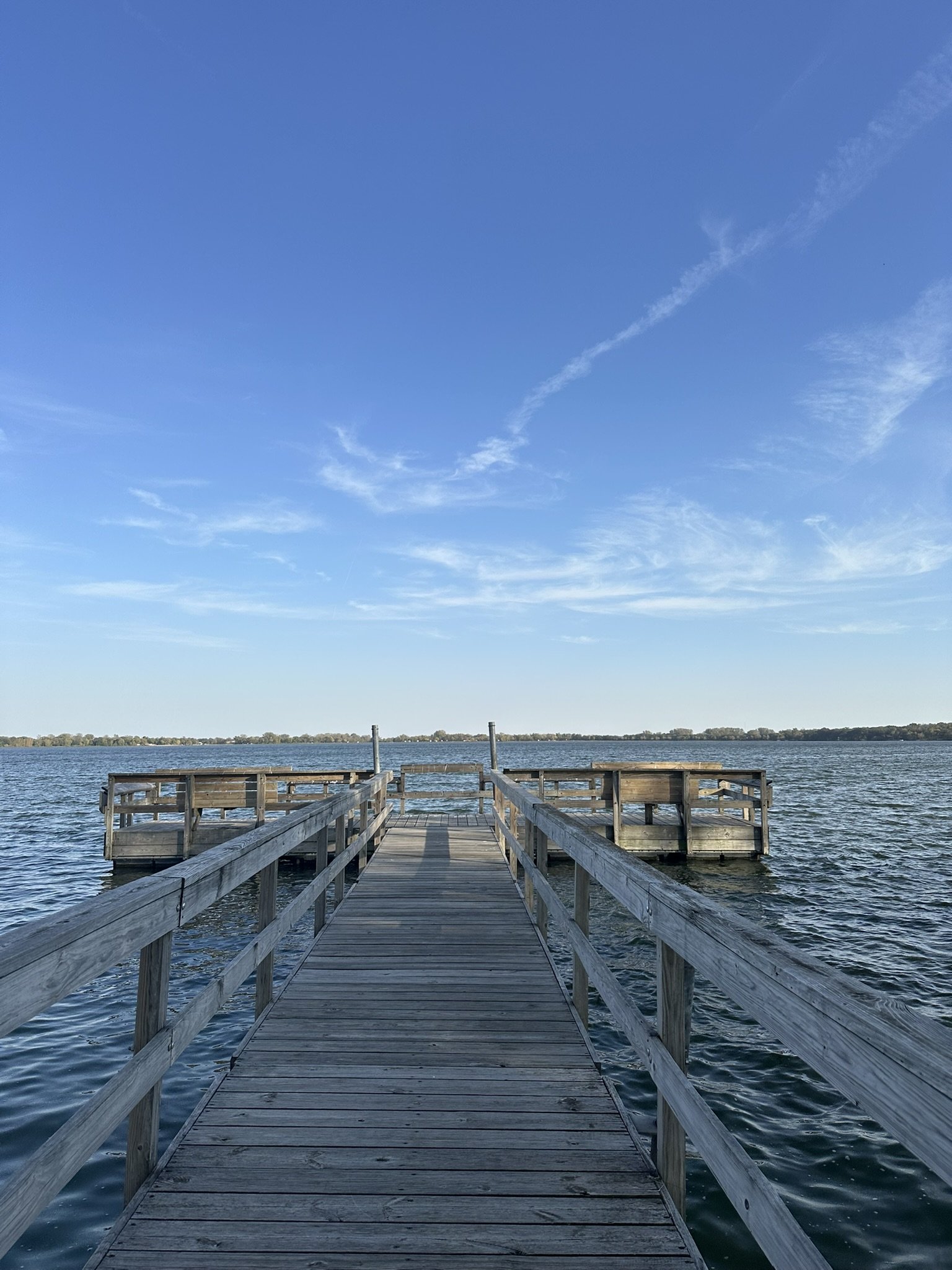 A wooden dock/fishing pier extending out over a body of water with a clear blue sky above.