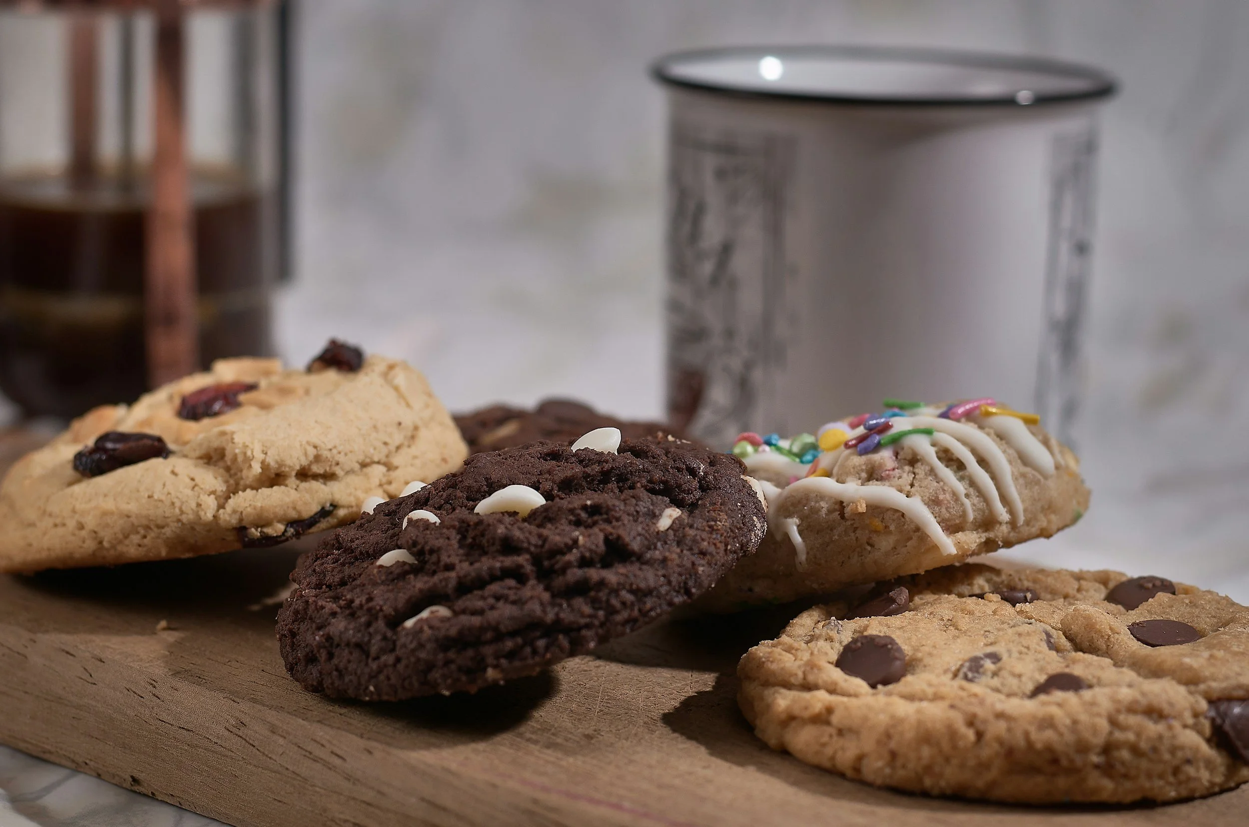 Assorted cookies on a wooden board with a metal container and a jar of dark syrup in the background.