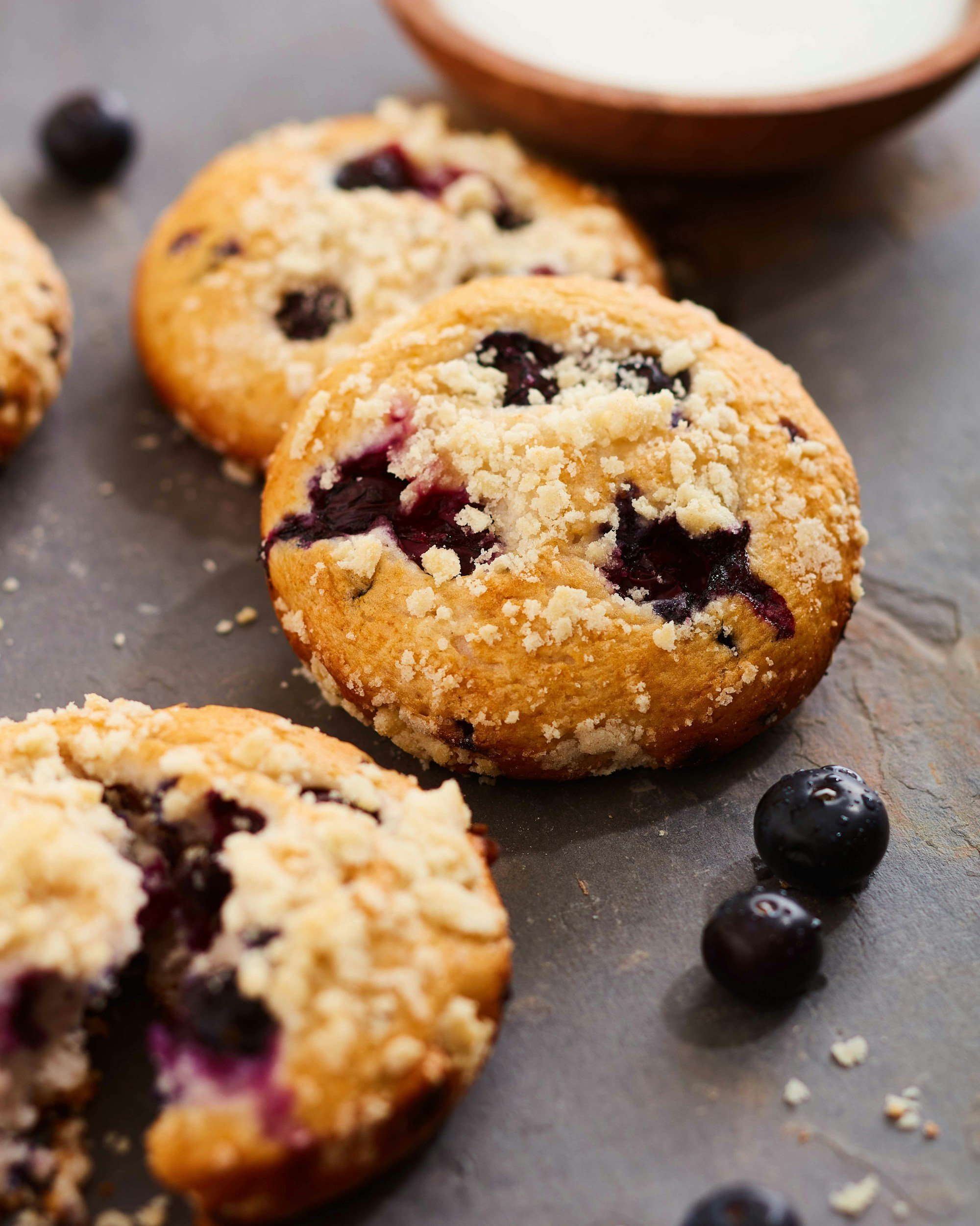 Close-up of blueberry muffins with crumb topping, with blueberries and a bowl in the background.