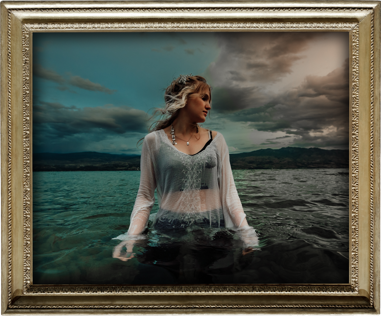 Quinn from Freeze The Fall standing in water, wearing a sheer white top and jewelry, with a lake, hills, and cloudy sky in the background.