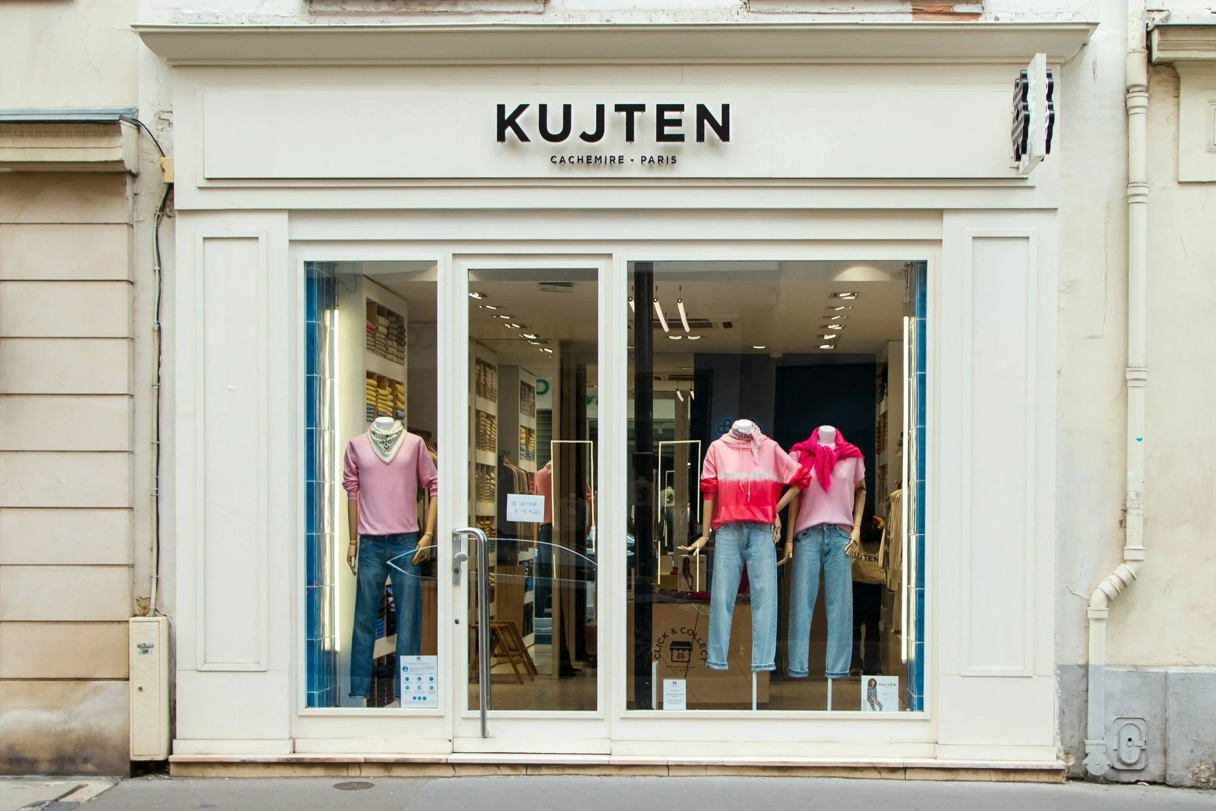 Front view of a clothing store named KUJTEN with mannequins dressed in pink and red tops and jeans in the window display.