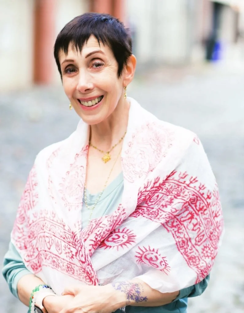 Ida Kenna, LPC, smiling warmly outdoors on a cobblestone street, wearing a light patterned shawl with red designs.