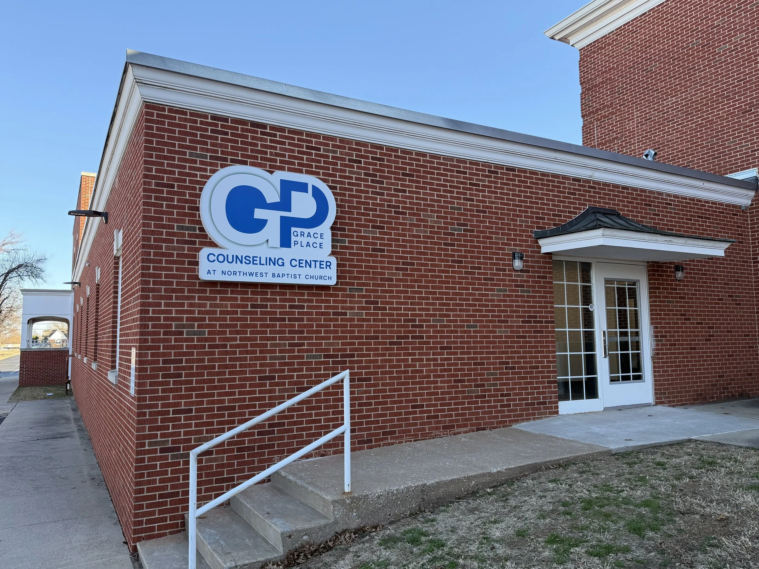 Brick building with a sign that reads 'Grace Place Counseling Center at Northwest Baptist Church' and a white door with glass panels.