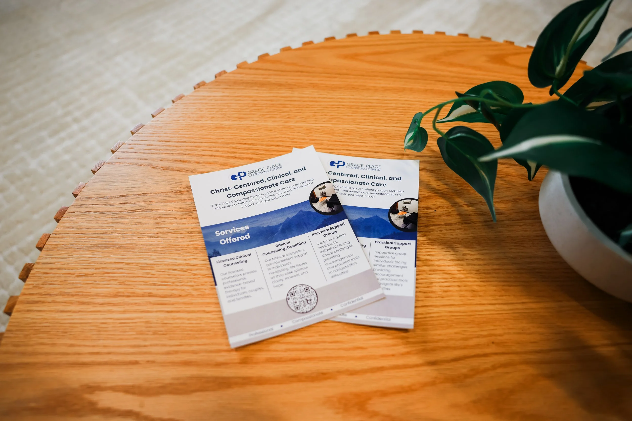 Brochures or flyers from Grace Place Counseling Center on a wooden table next to a potted plant.