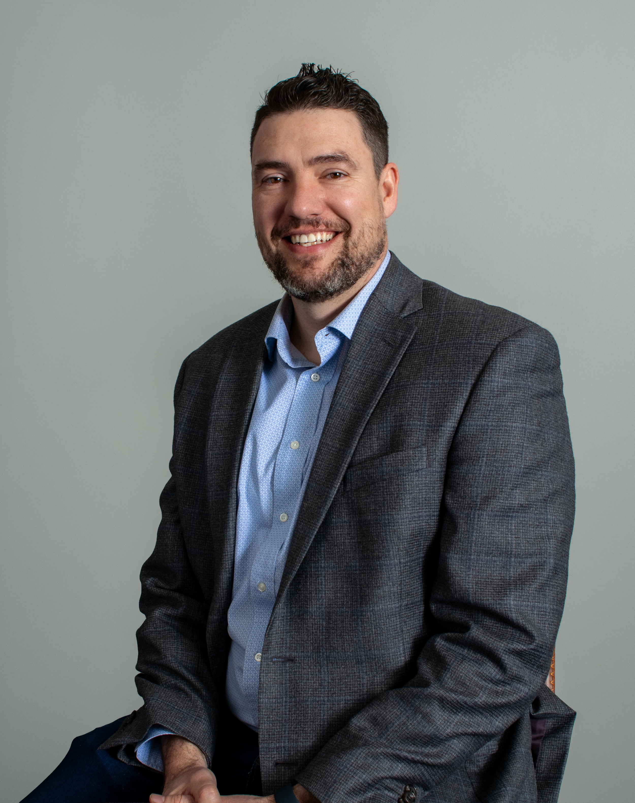 A smiling man and woman taking a selfie together outdoors with a brick building and a window in the background.