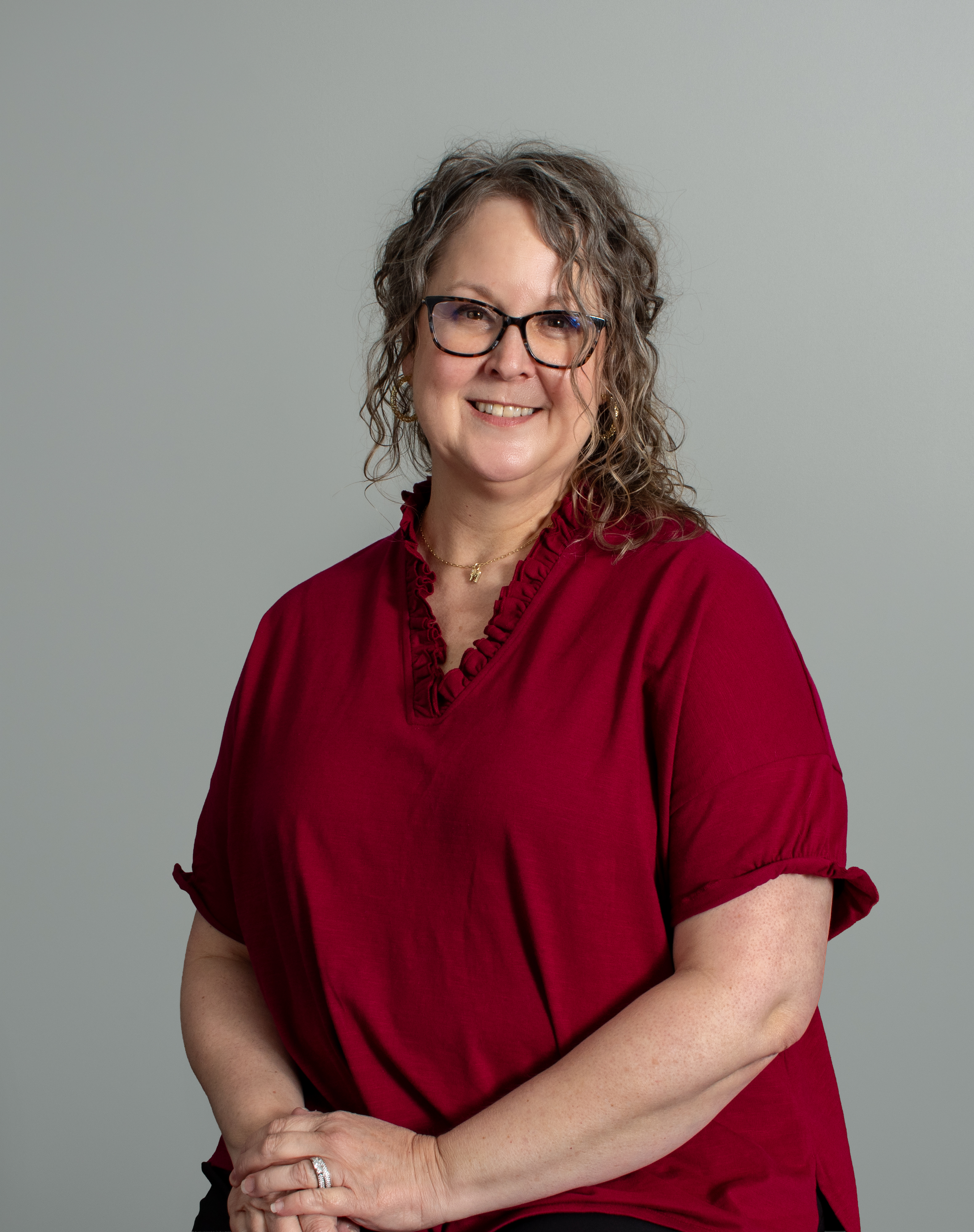 A woman with short, curly blonde hair smiling outdoors with steps in the background.
