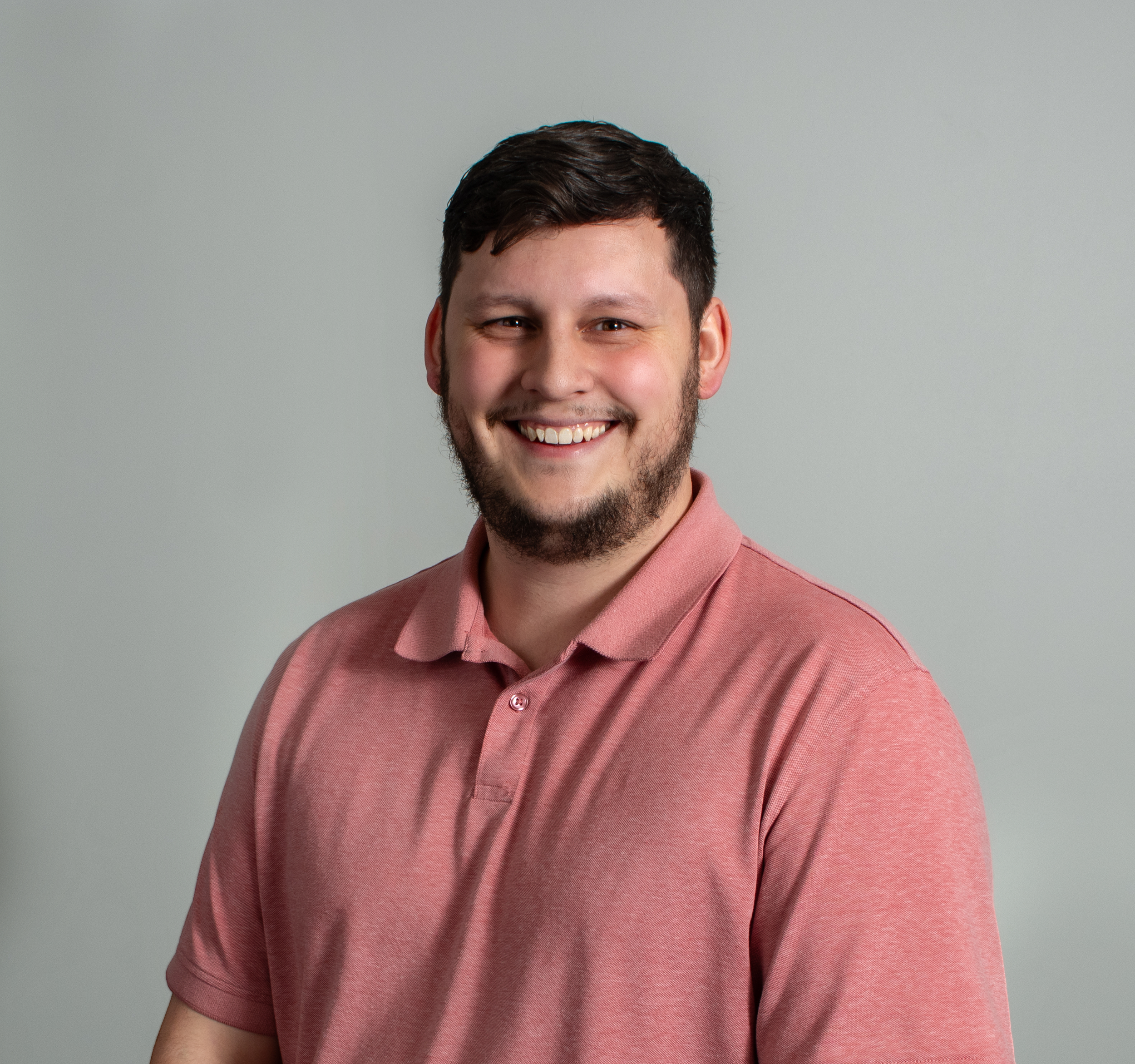 A family of three standing on a lawn in front of a brick house with large windows. The woman is holding a young boy. The family is smiling, and trees and shrubs are visible around them.