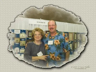 A woman and a man smiling at a photo event, standing in front of display cases with awards or plaques.