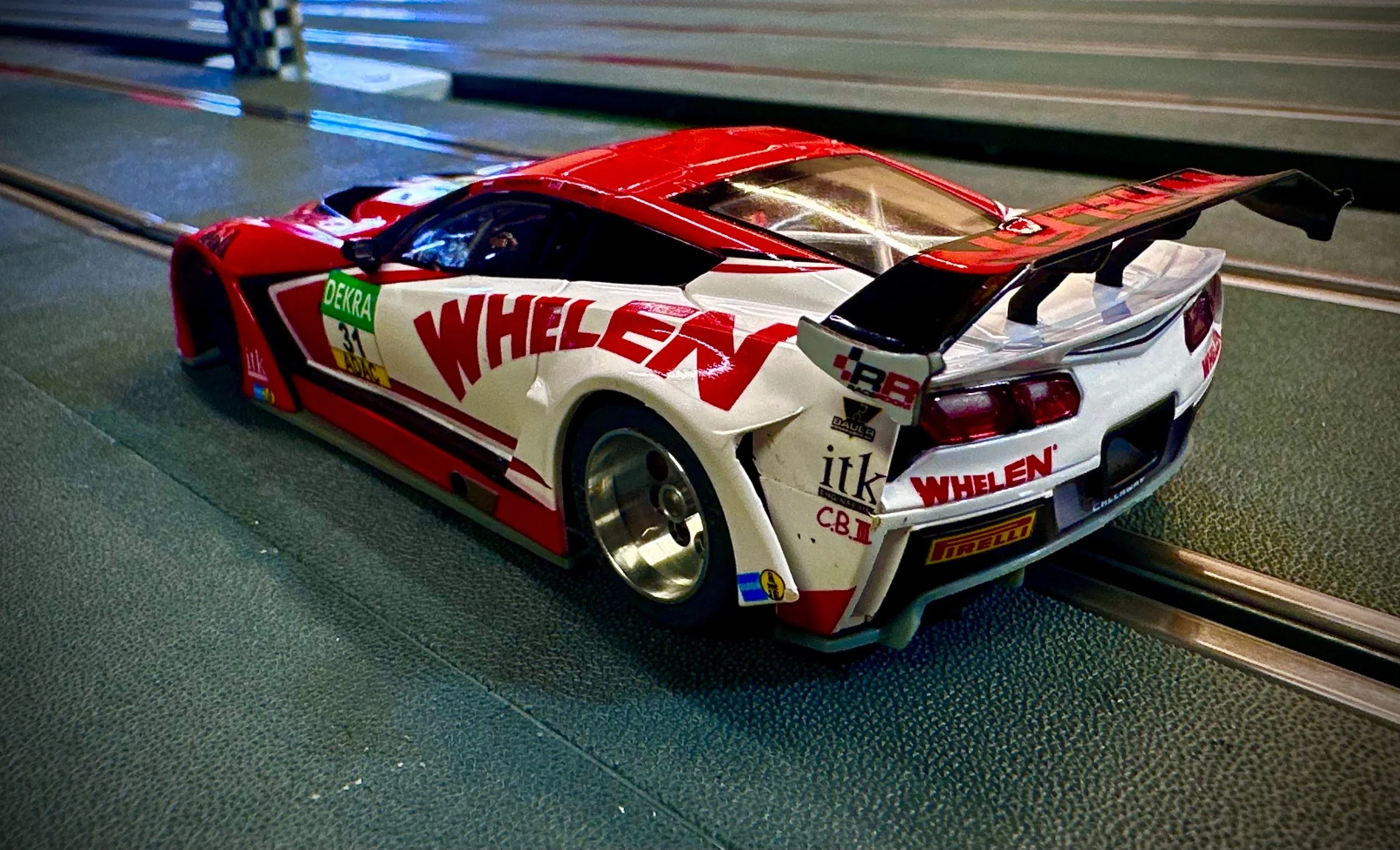 A detailed view of a race car on a slot car track, featuring decals and sponsor logos, with a prominent rear wing.