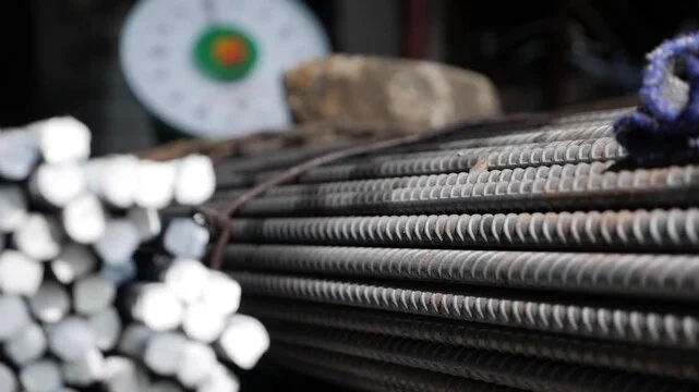 Close-up of stacked steel rebar with a concrete weight and a blurred circular object in the background.