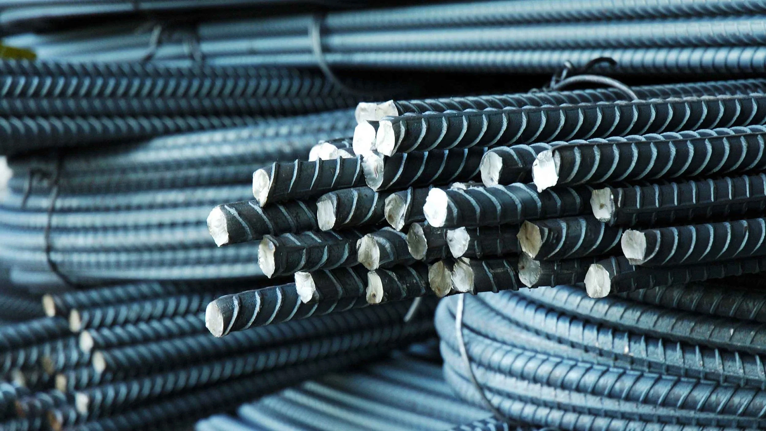 Close-up of black steel rebar stacked together, used in construction for reinforcement.