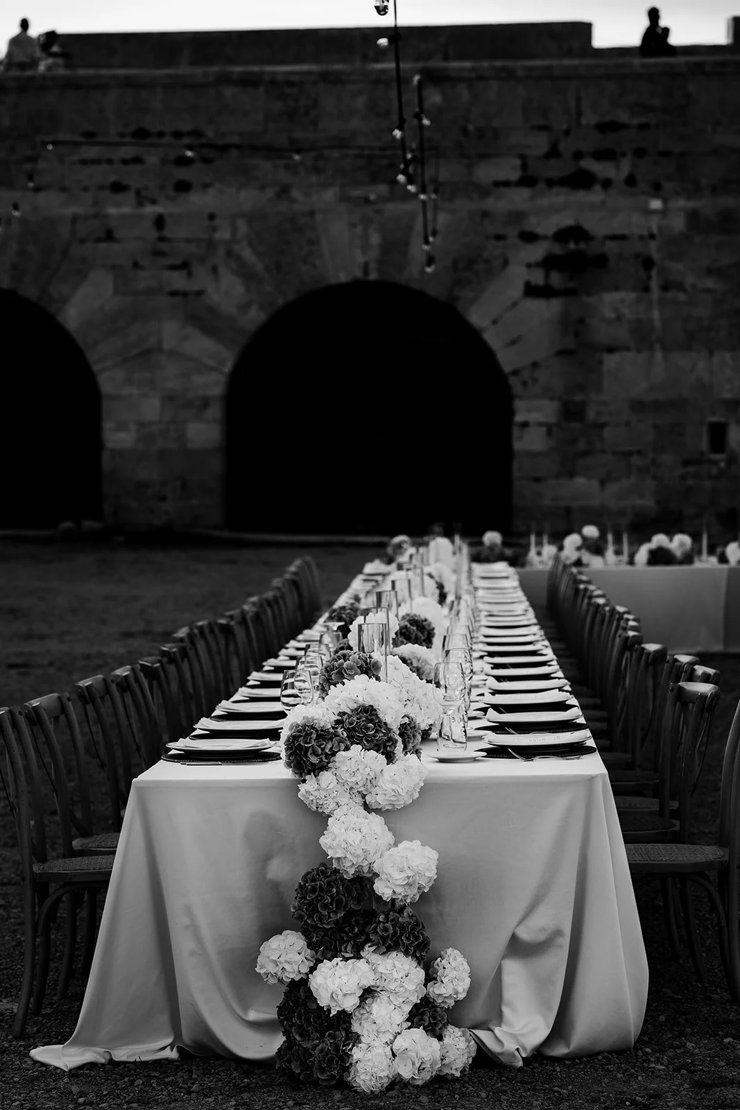 Editorial black and white image of a long wedding table with floral arrangements in a historic venue