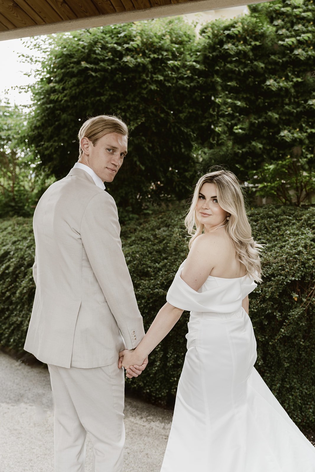Braut und Bräutigam blicken beim gemeinsamen Spaziergang während ihrer Hochzeit in die Kamera.