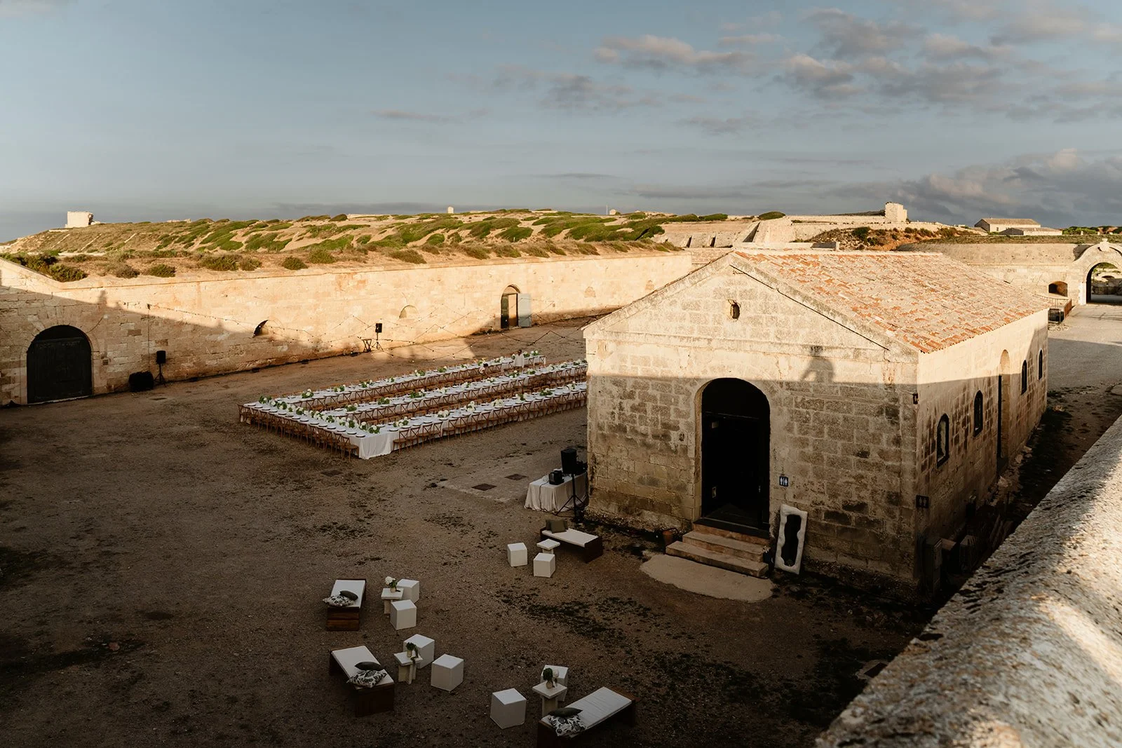 Elegant wedding dinner setup inside a historic fort in Menorca with long tables and minimal styling