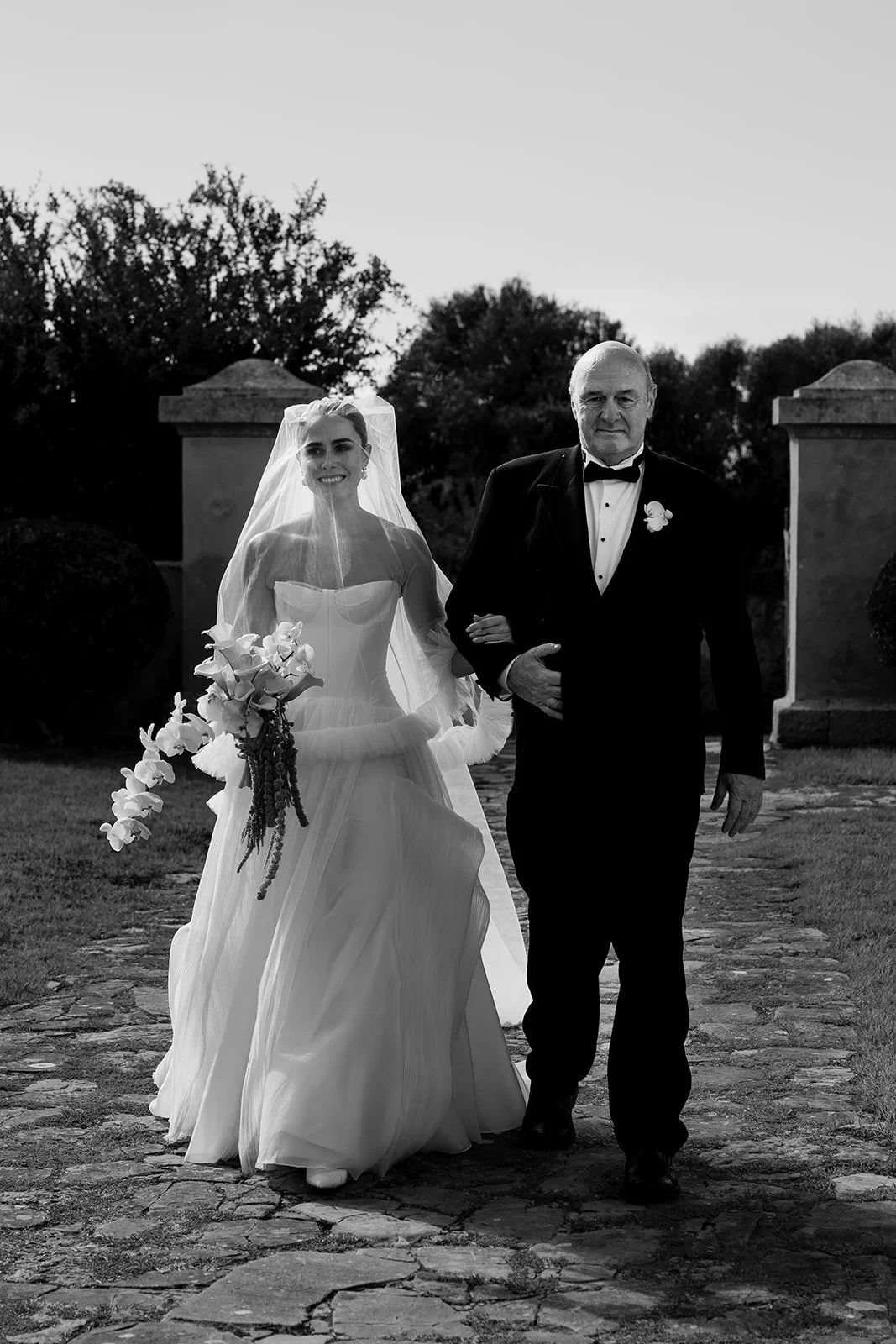 Bride walking with her father toward the ceremony in an intimate black and white moment