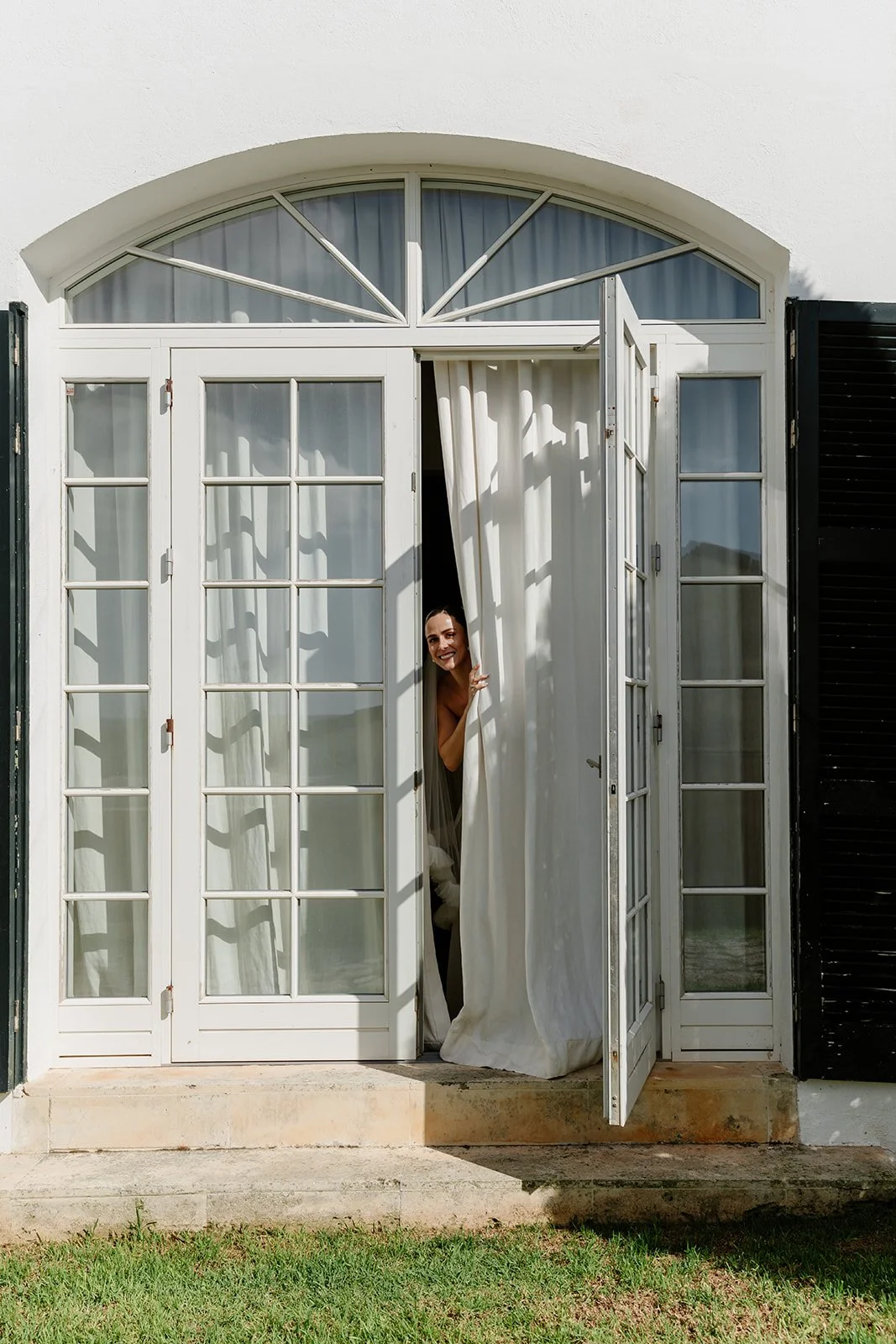 Bride looking through curtains during getting ready at Menorca wedding